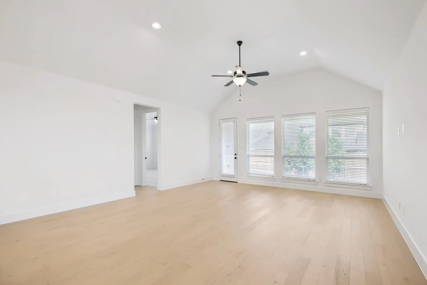 Spacious room featuring vaulted ceilings, light wood-finish flooring, recessed lighting, a ceiling fan, and multiple windows with blinds