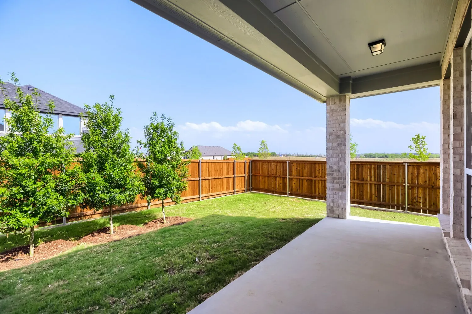 Covered patio with concrete flooring, brick columns, and a flush-mount outdoor light fixture
