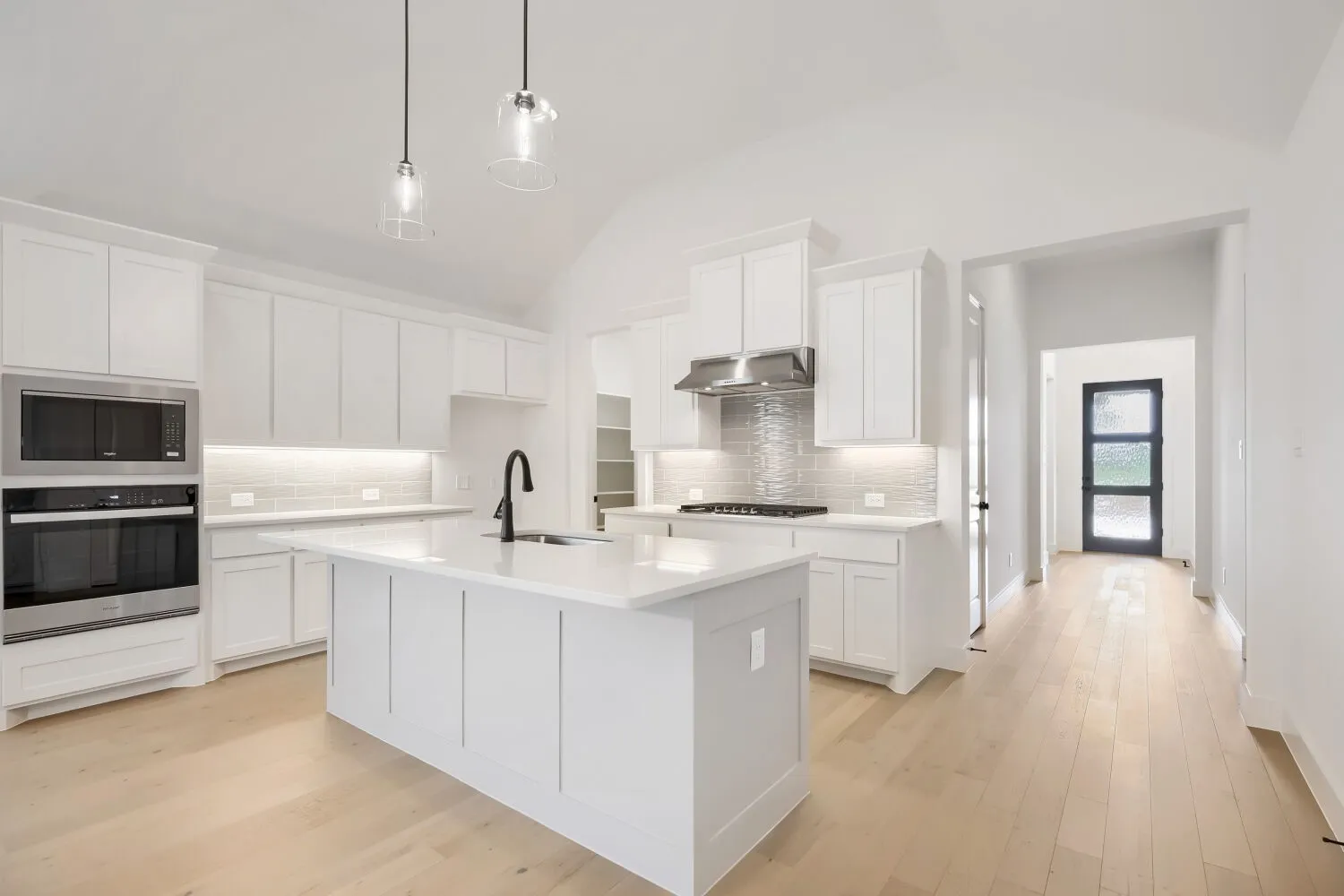 Kitchen featuring a large central island with a sink, white cabinetry, integrated stainless steel appliances, light wood-finish flooring, and pendant lighting