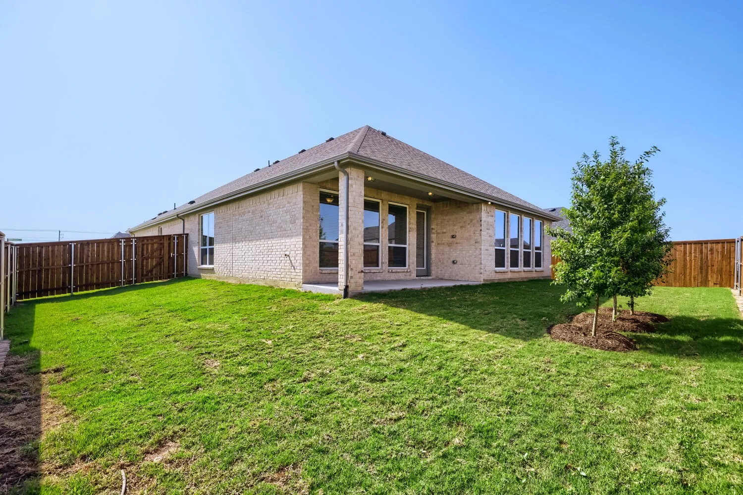 Expansive backyard featuring a manicured lawn, established trees, and a wooden privacy fence