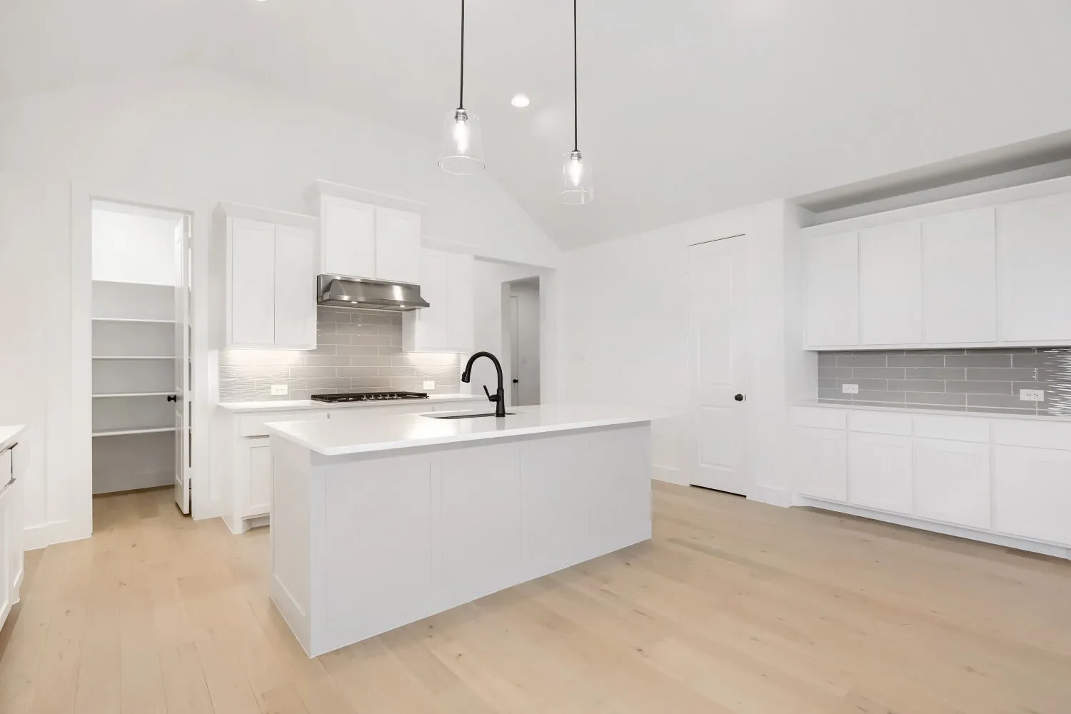 Modern kitchen featuring a central island, light wood-finish flooring, white cabinetry, a subway tile backsplash, and vaulted ceilings