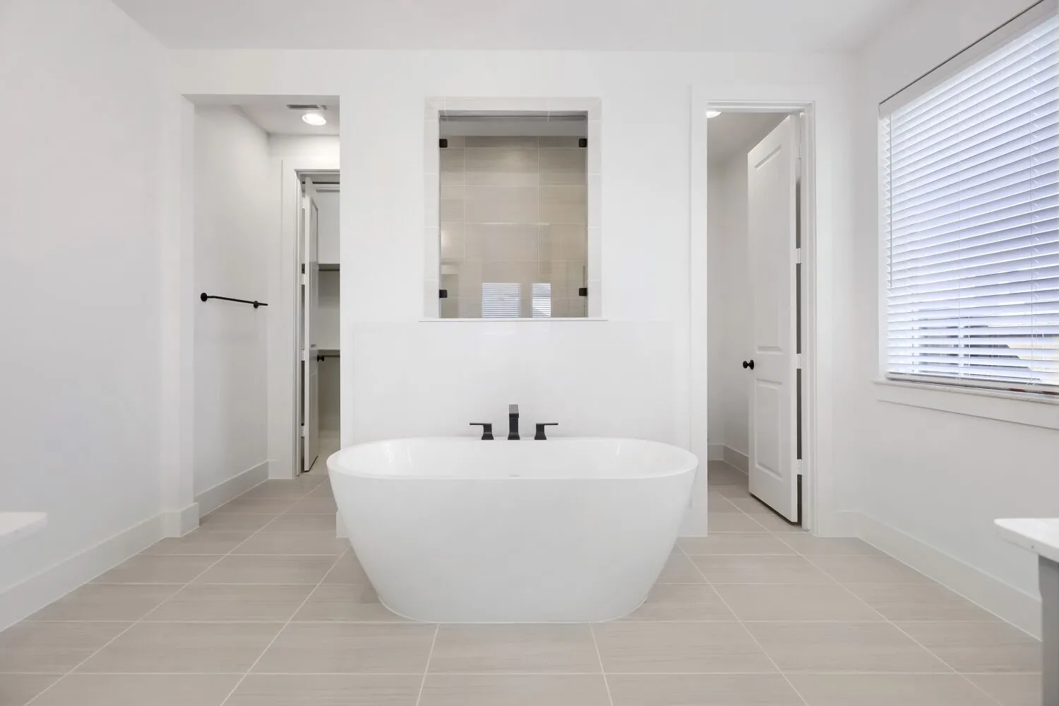 Freestanding soaking tub with matte black fixtures, set against light-toned tile flooring