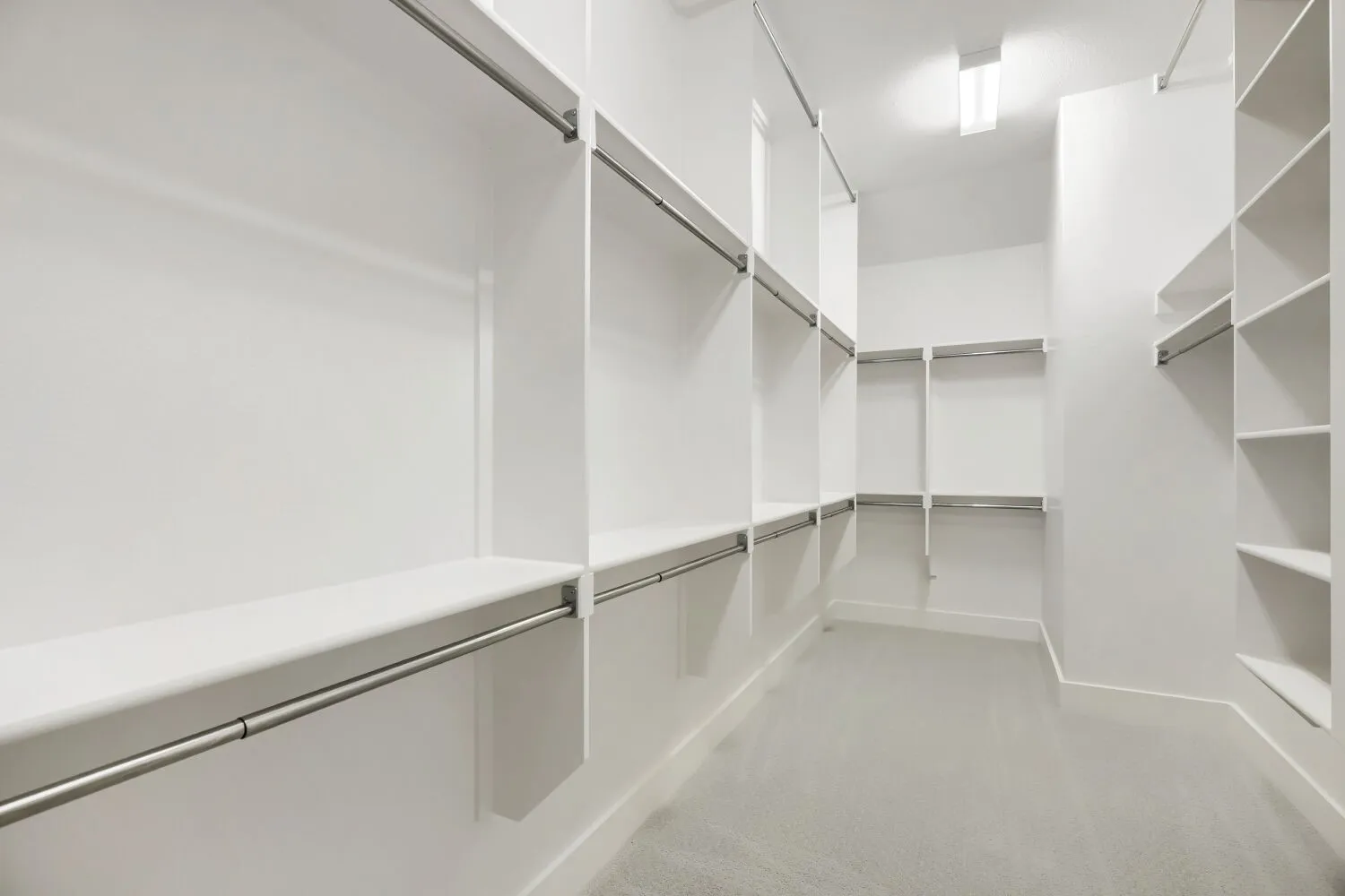 Spacious walk-in closet featuring extensive built-in shelving, multiple hanging rods, recessed lighting, white walls, and light-toned carpet flooring