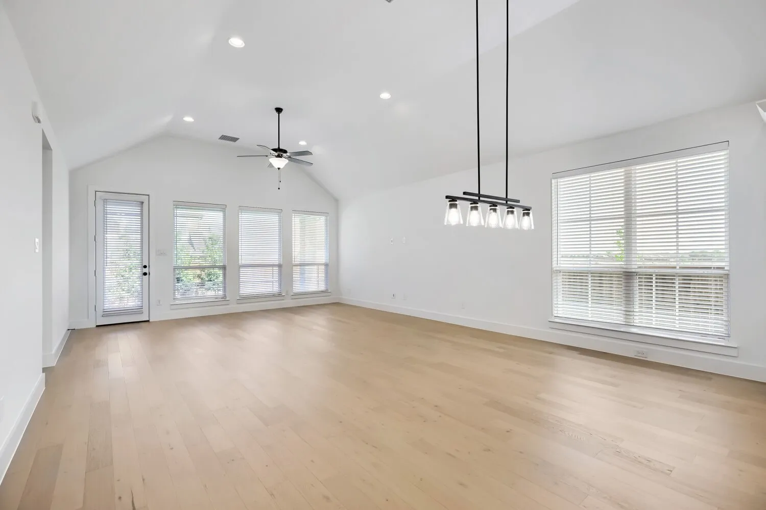 Spacious room featuring light wood-finish flooring, a vaulted ceiling, and multiple windows