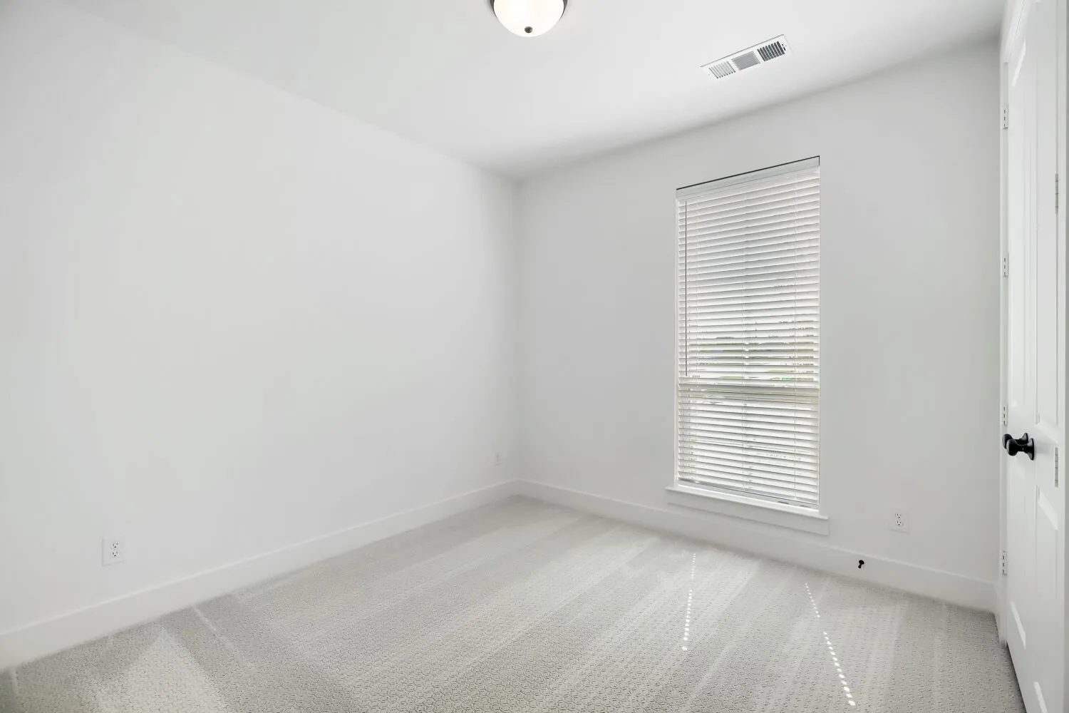 Carpeted interior room featuring a single window with horizontal blinds, white baseboards, and a flush-mount ceiling light