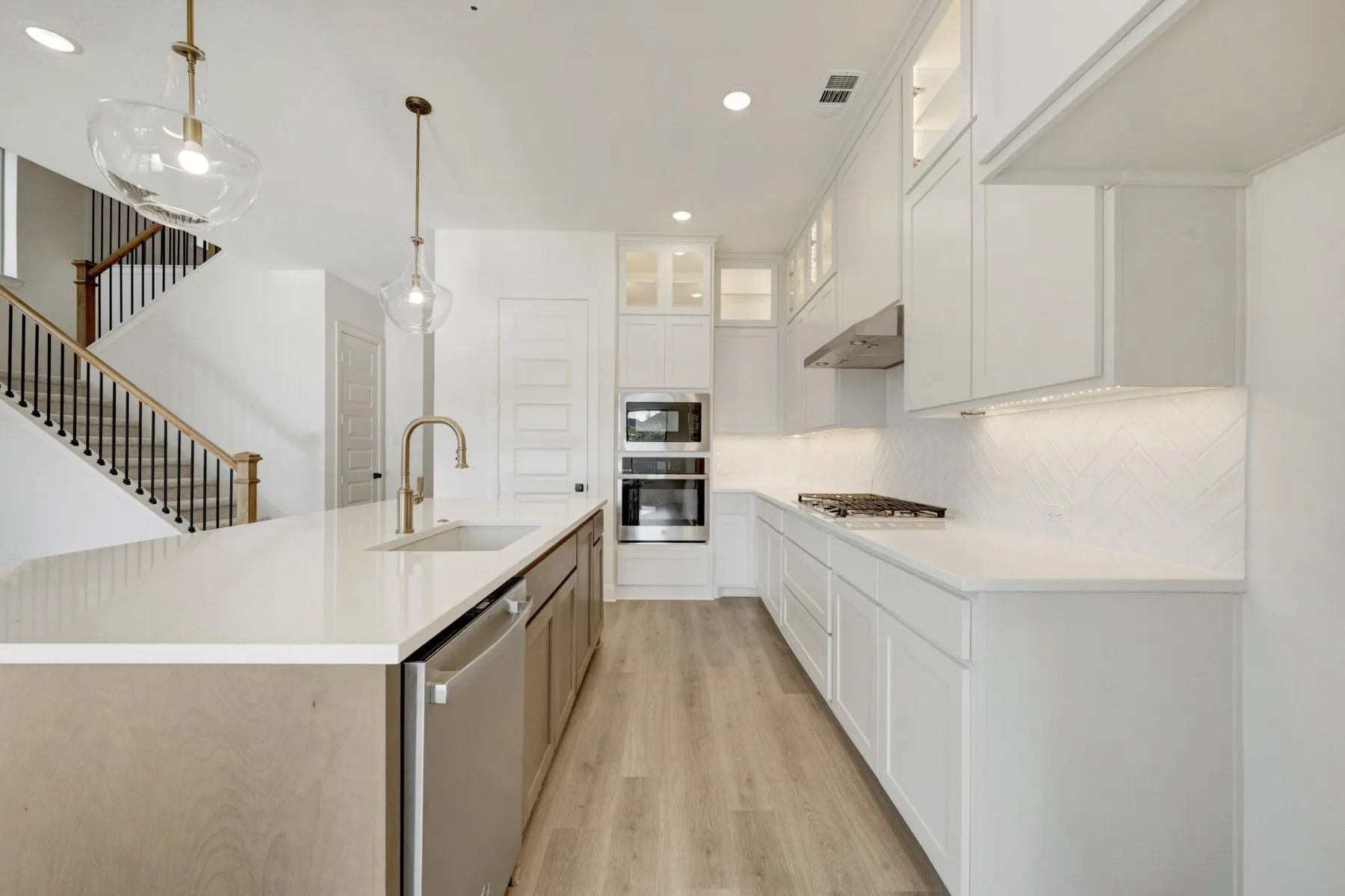 Modern kitchen featuring a large central island with an undermount sink, stainless steel dishwasher, and contemporary pendant lighting
