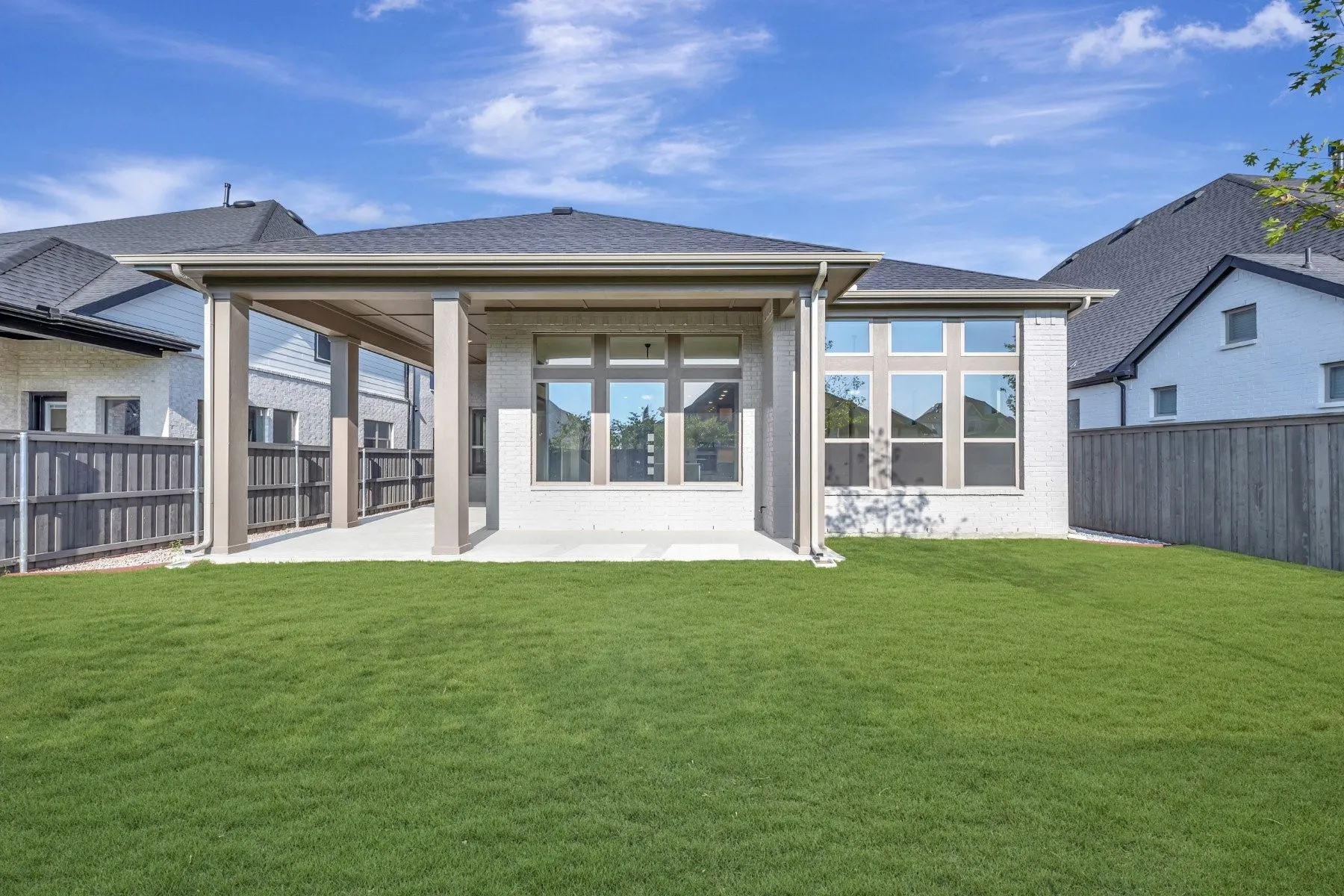 Expansive backyard with a covered patio, brick exterior, multiple windows, and a privacy fence