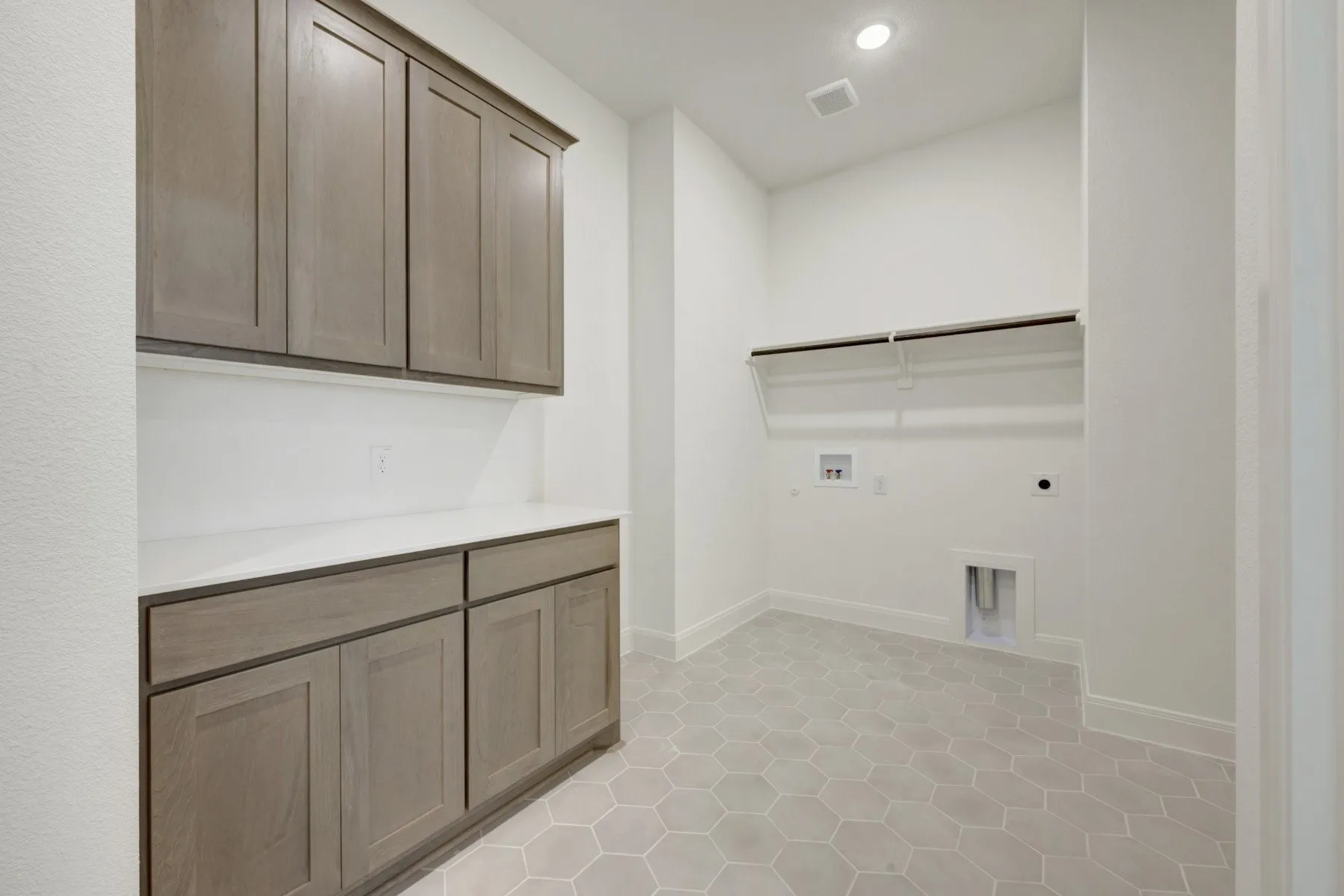 Laundry room featuring hexagonal floor tiling, custom cabinetry with a counter surface, and built-in shelving