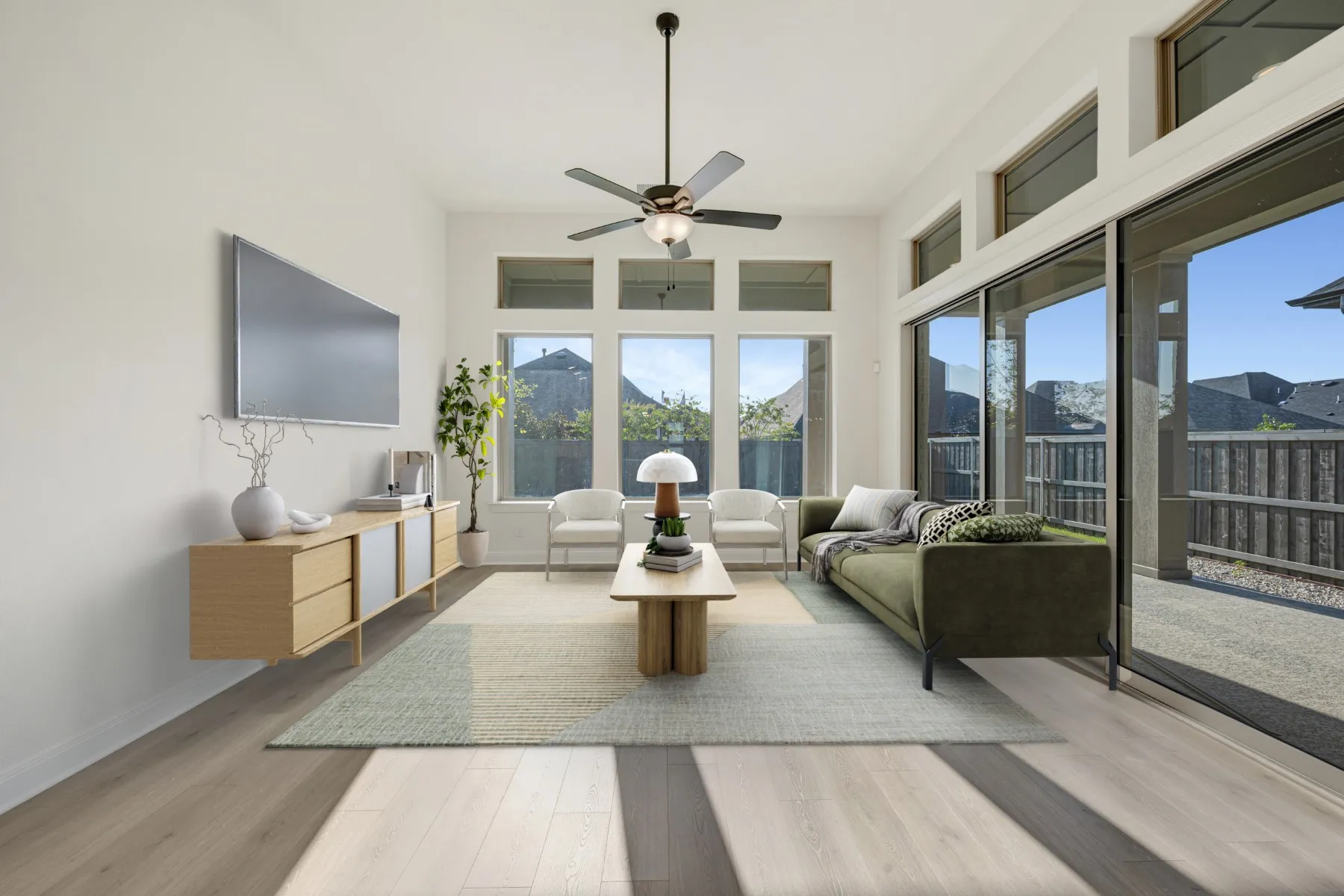 Spacious living area featuring high ceilings, wood-finish flooring, a ceiling fan, and extensive natural light from multiple windows