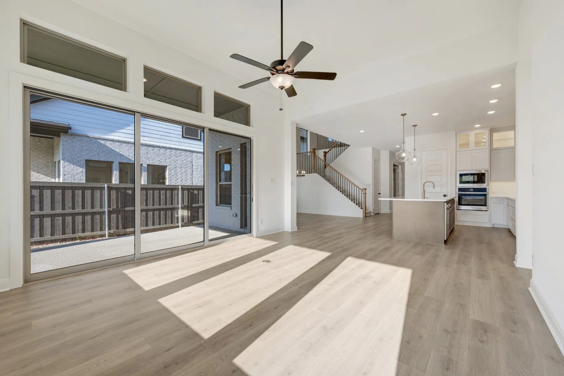 Open-concept living area with wood-finish flooring, a contemporary ceiling fan, and large sliding glass doors
