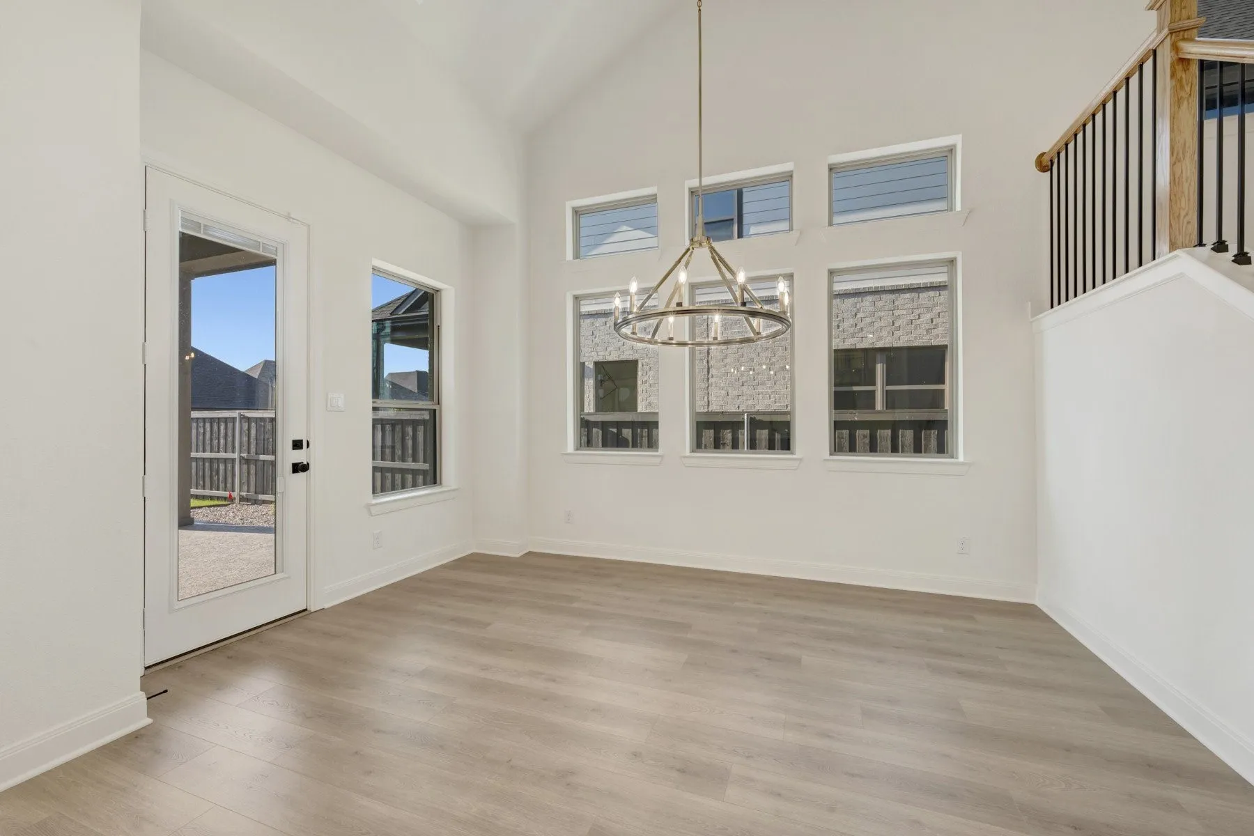 Spacious room featuring high vaulted ceilings, multiple windows providing abundant natural light, wood-finish flooring, and a contemporary chandelier