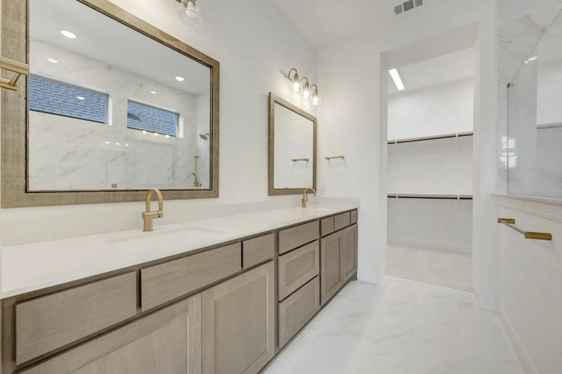 Dual vanity with light wood-finish cabinetry, white countertops, and gold-toned fixtures