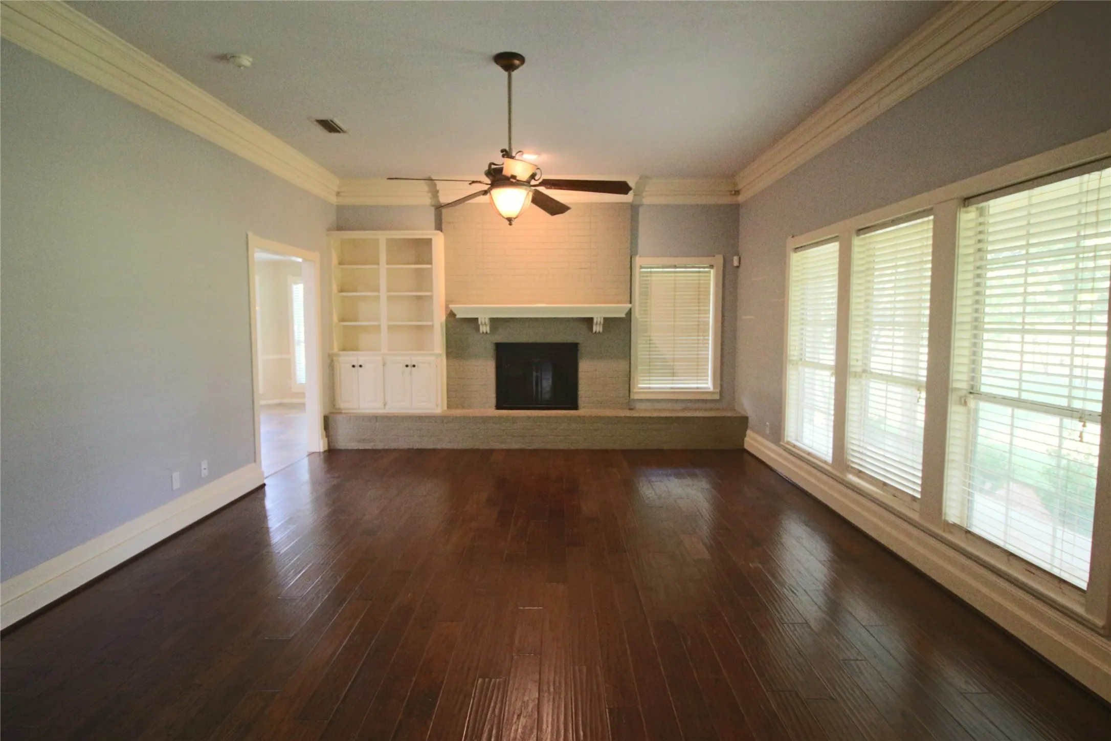 Living room featuring ornamental molding, a brick fireplace, dark wood look flooring, and a ceiling fan