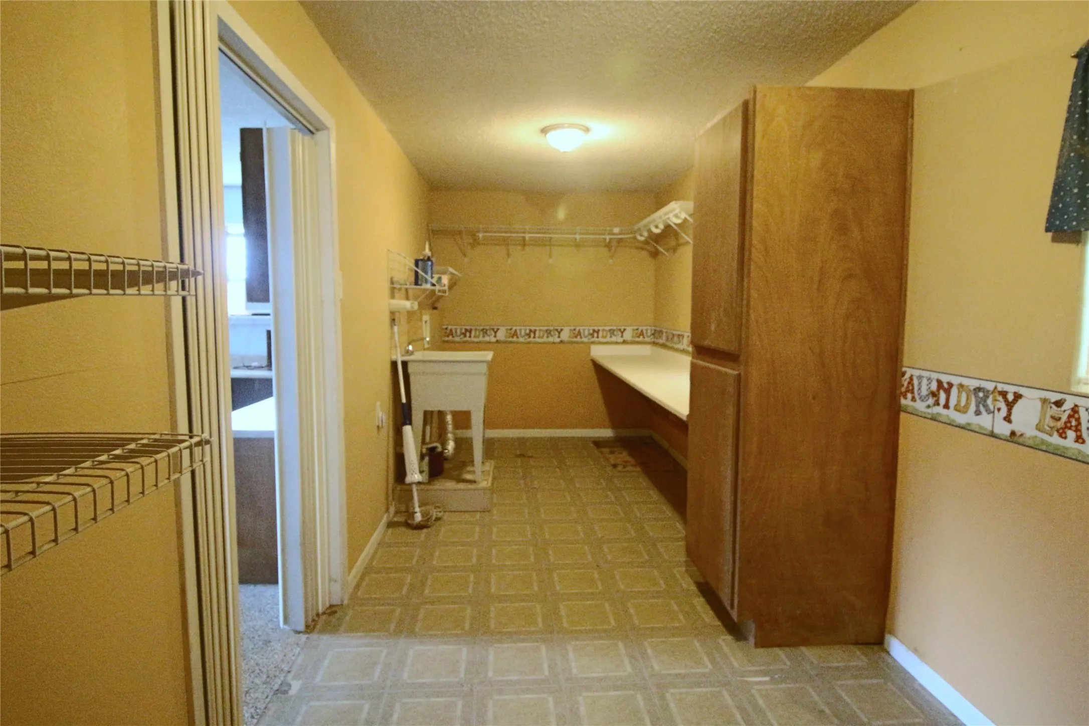 Spacious laundry area with sink, counter top, cabinets and hanging rods.