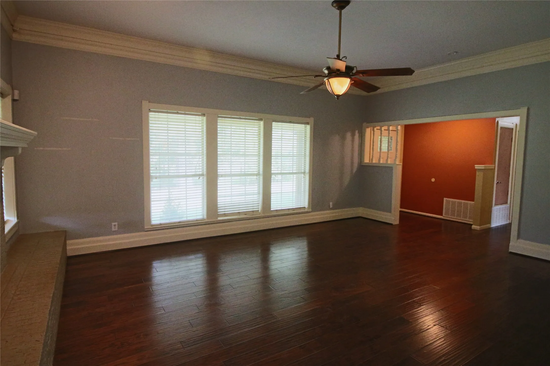 Living room with crown molding, dark wood look floors, a fireplace, ceiling fan, and built in shelves
