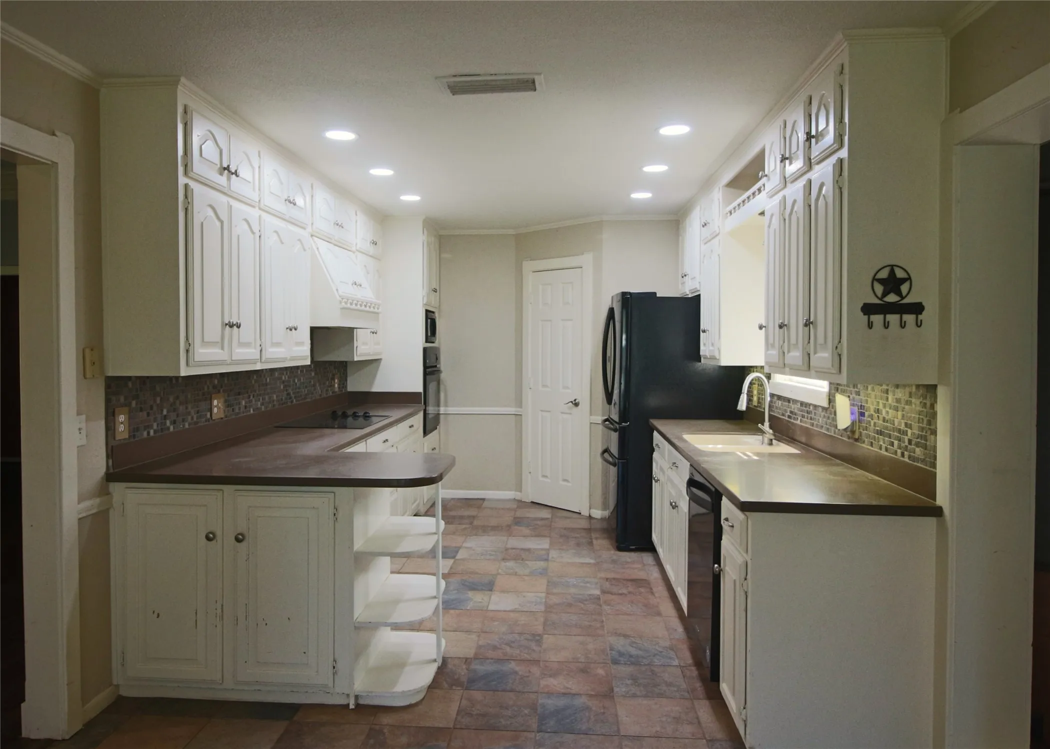 Kitchen with white cabinetry, black appliances, decorative backsplash and black appliances.