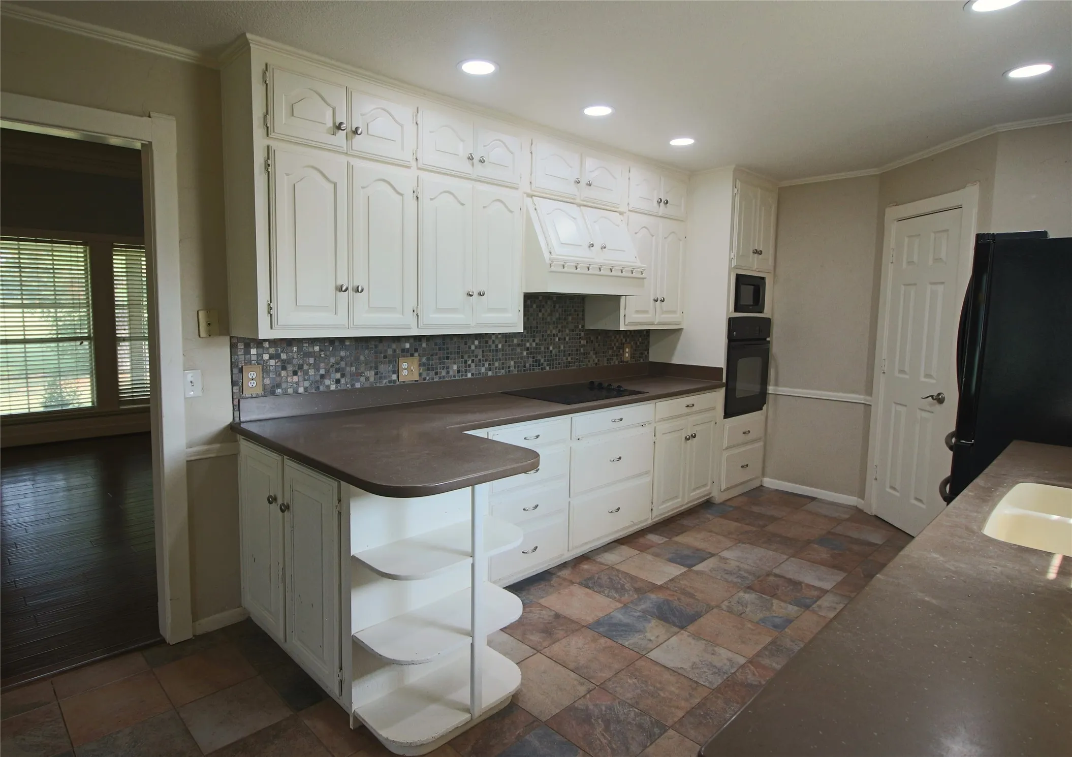 Kitchen featuring dark countertops, white cabinets, black appliances, decorative backsplash, and recessed lighting