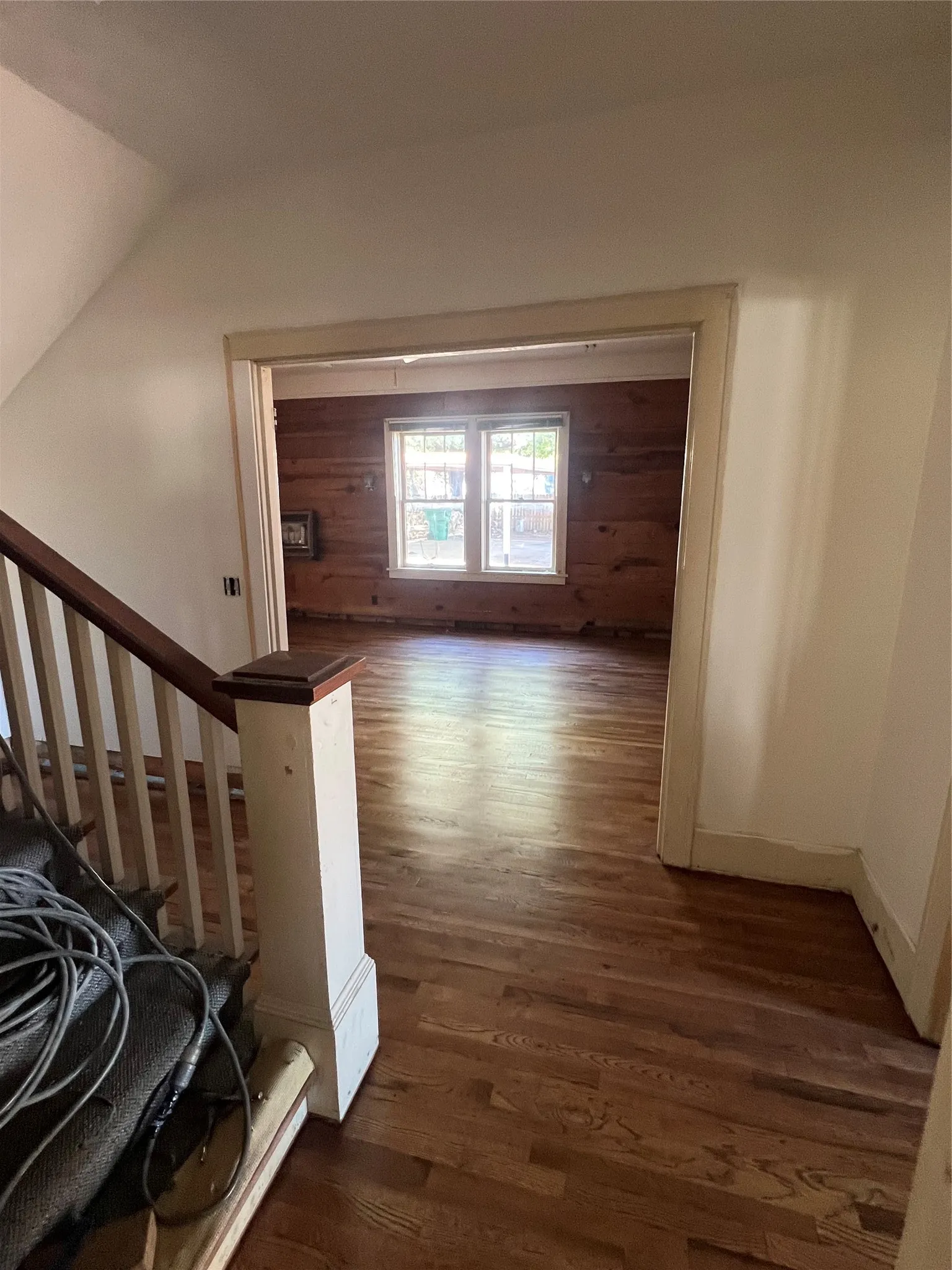 Hardwood flooring throughout, with a wood-paneled accent wall, and a traditional staircase featuring a wood handrail