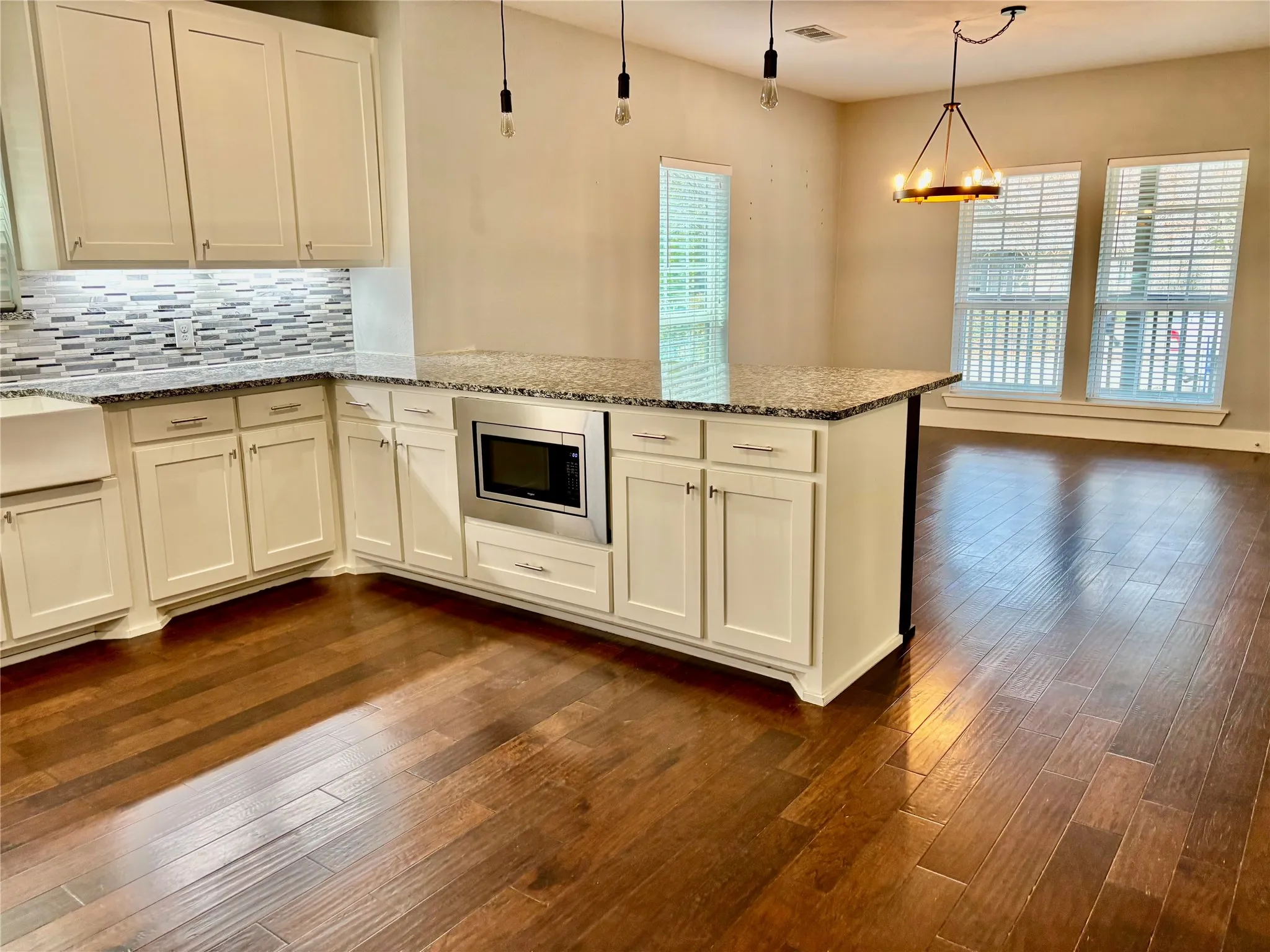 Kitchen with light stone countertops, tasteful backsplash, a peninsula, dark wood-type flooring, and stainless steel microwave