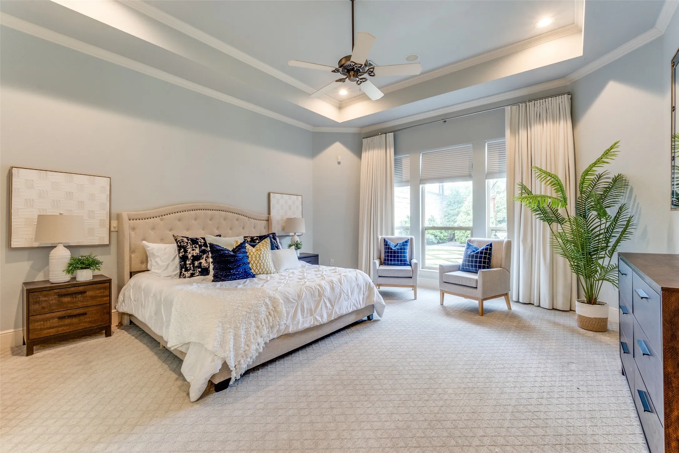 Bedroom with light colored carpet, ornamental molding, a raised ceiling, and ceiling fan