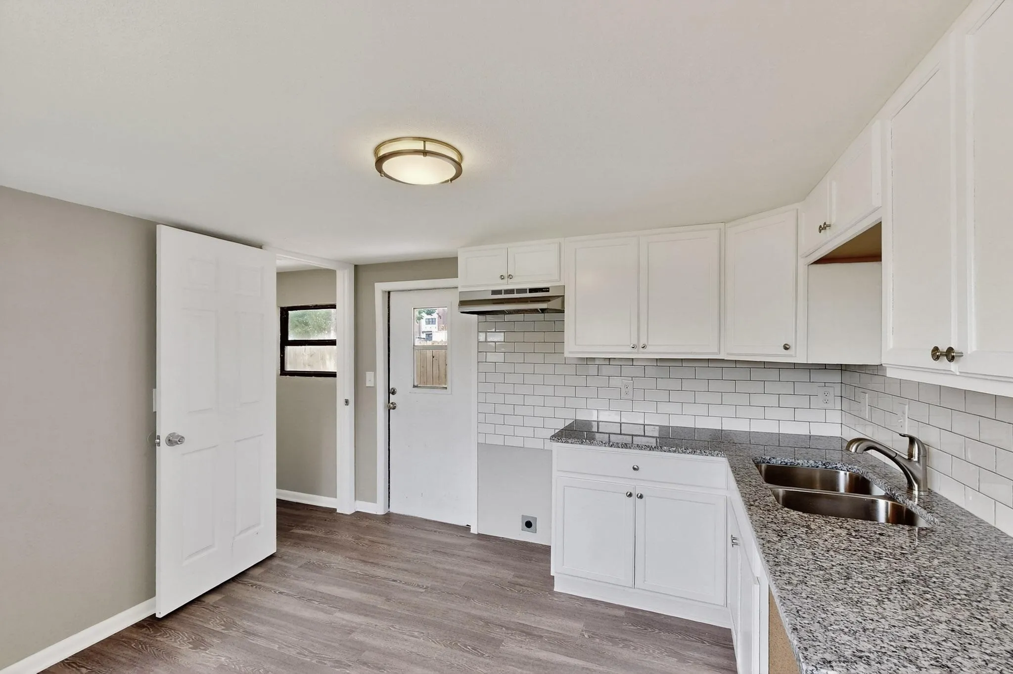 Kitchen featuring light stone countertops, white cabinets, light wood-type flooring, and decorative backsplash