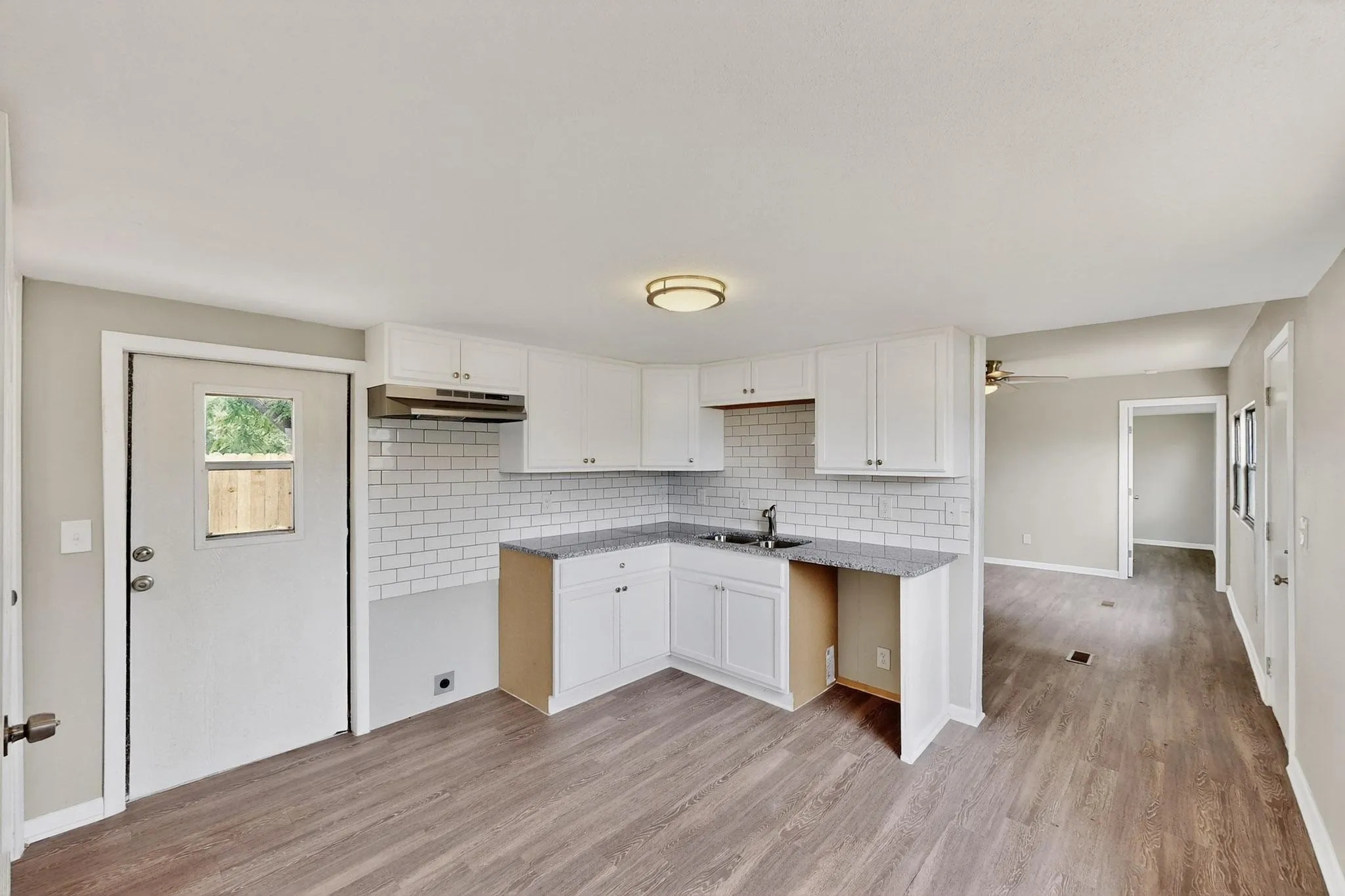 Kitchen featuring white cabinetry, light wood finished floors, backsplash, ceiling fan, and light stone counters