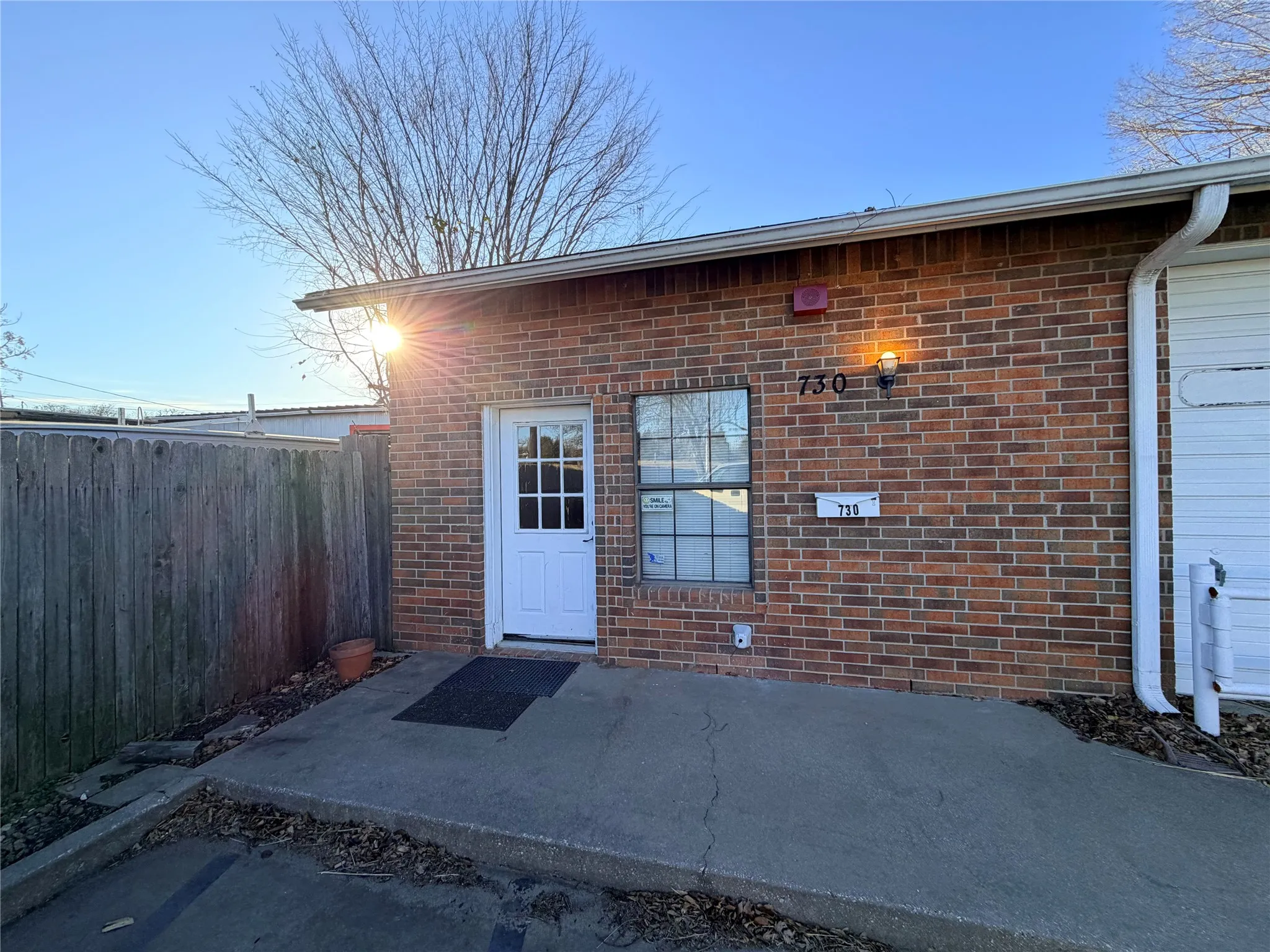 Exterior entry area with a wooden privacy fence and a concrete walkway leading to the door.