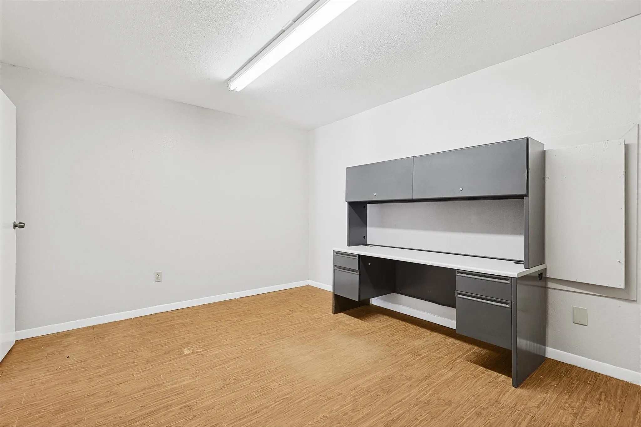 Unfurnished office featuring built in desk, a textured ceiling, and light wood-type flooring