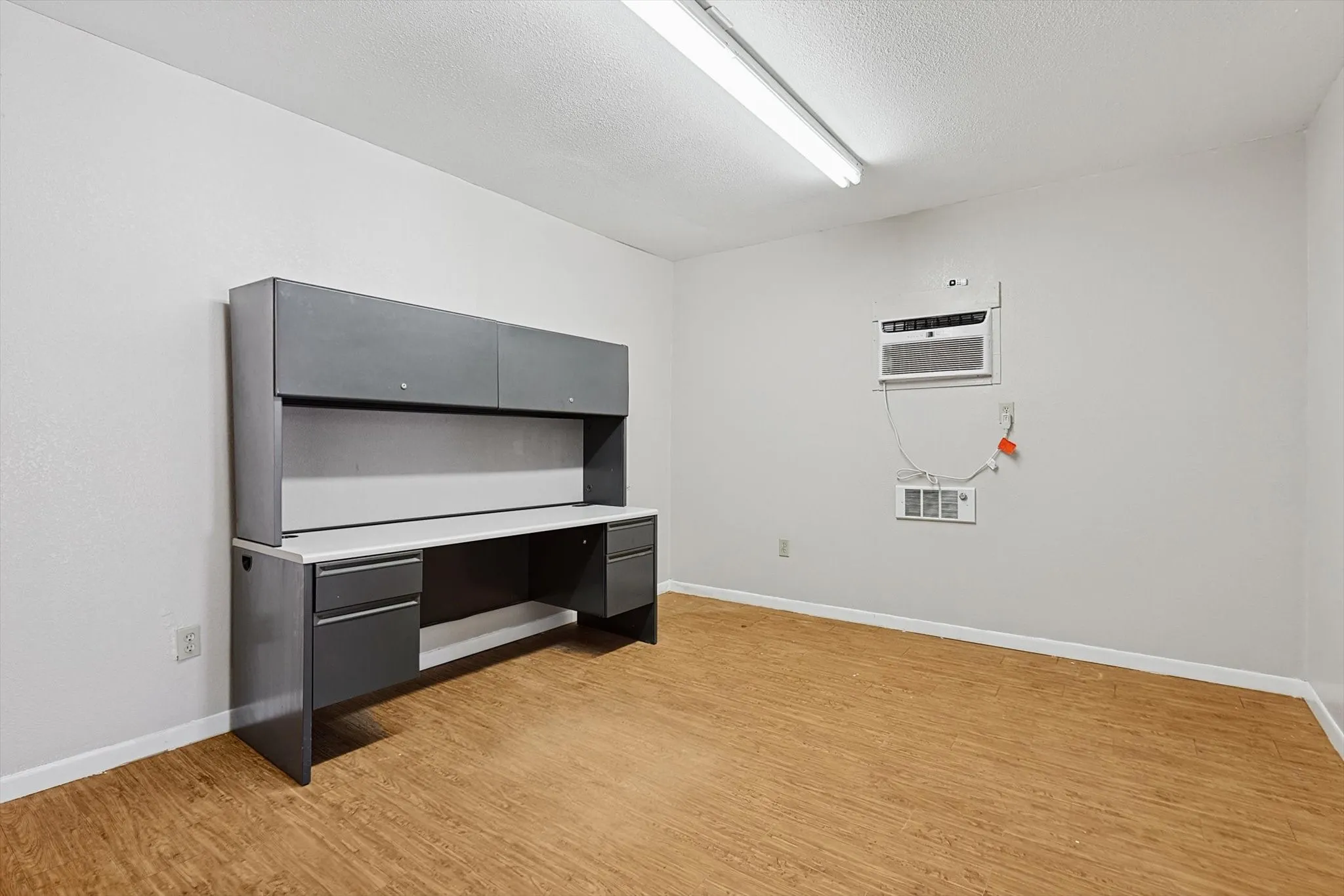 Unfurnished office featuring a textured ceiling, a wall mounted AC, and light hardwood / wood-style flooring
