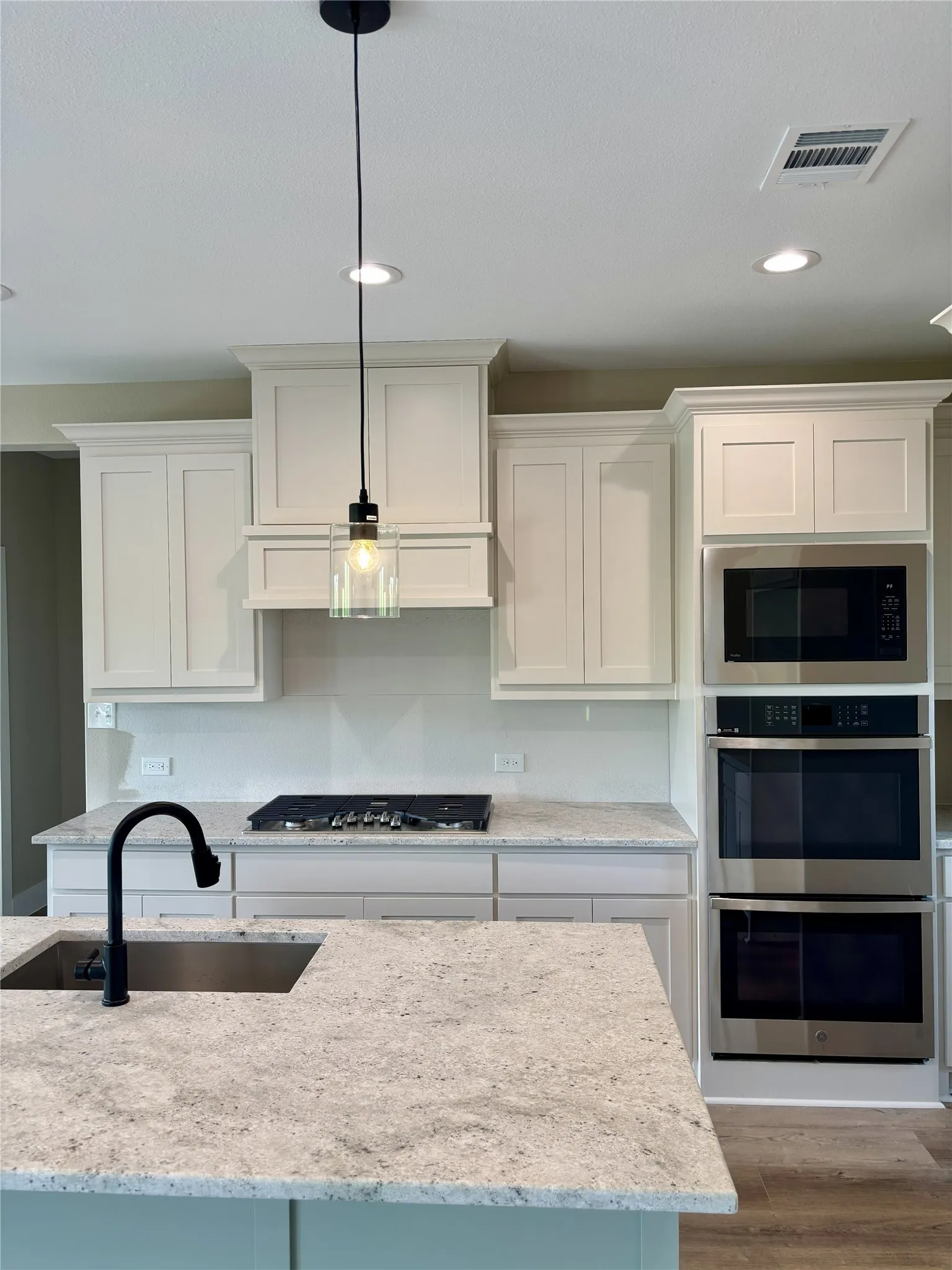 Kitchen with light stone countertops, stainless steel appliances, white cabinets, and decorative light fixtures