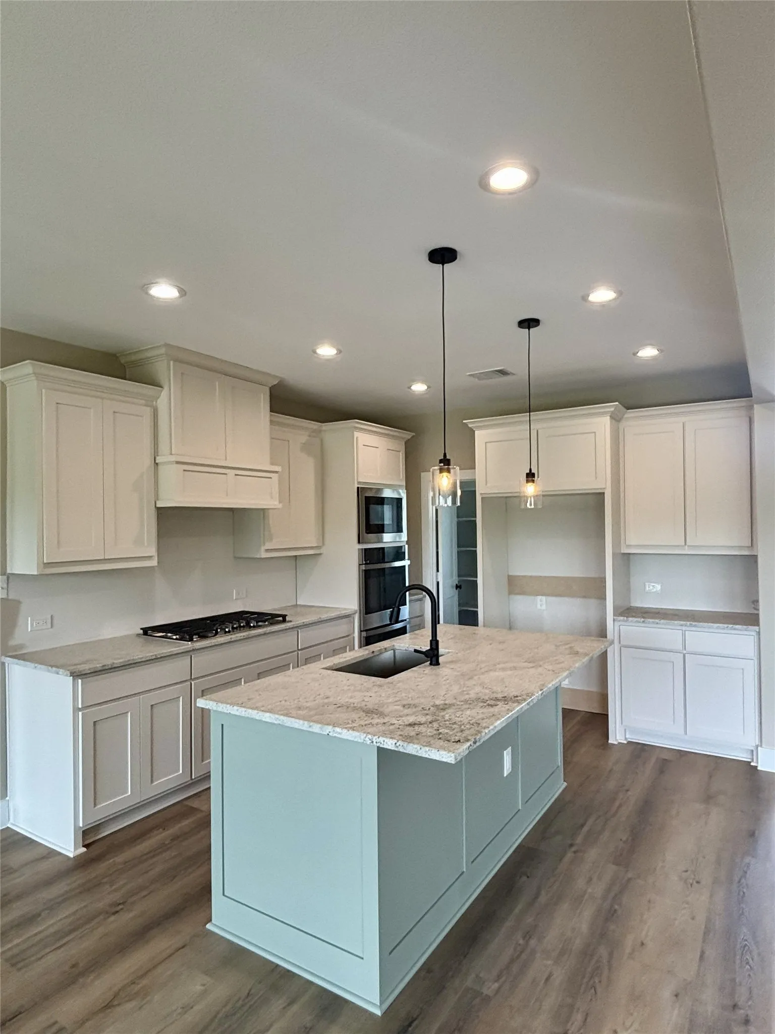 Kitchen featuring light stone counters, dark wood-style flooring, white cabinetry, an island with sink, and pendant lighting
