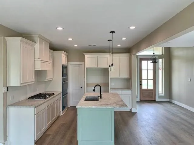 Kitchen featuring an island with sink, dark wood finished floors, pendant lighting, light stone counters, and stainless steel gas cooktop