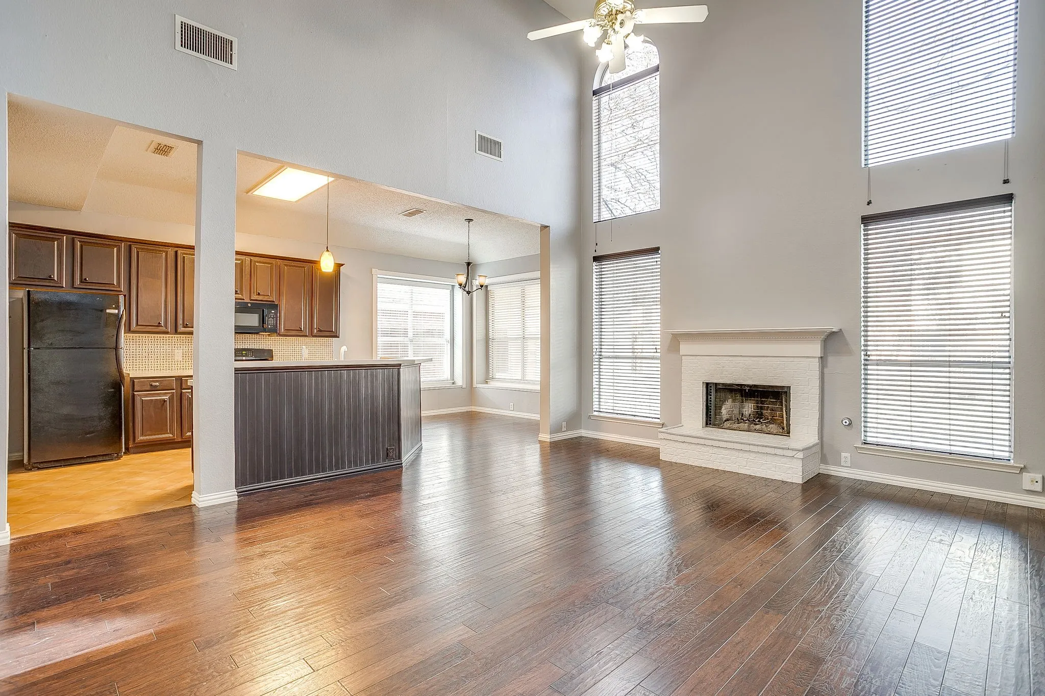 Unfurnished living room with dark wood-style flooring, a ceiling fan, hanging lights, a high ceiling, and a brick fireplace