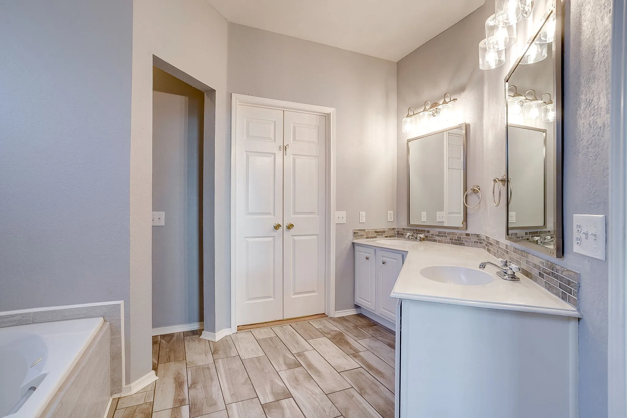 Full bath with vanity, wood finish floors, and a relaxing tiled tub