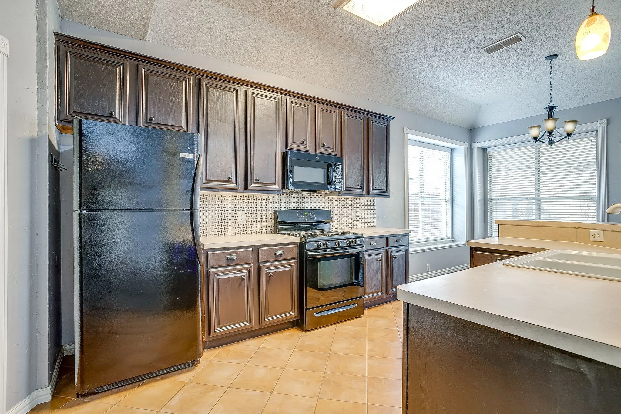 Kitchen featuring black appliances, light countertops, decorative backsplash, and a chandelier