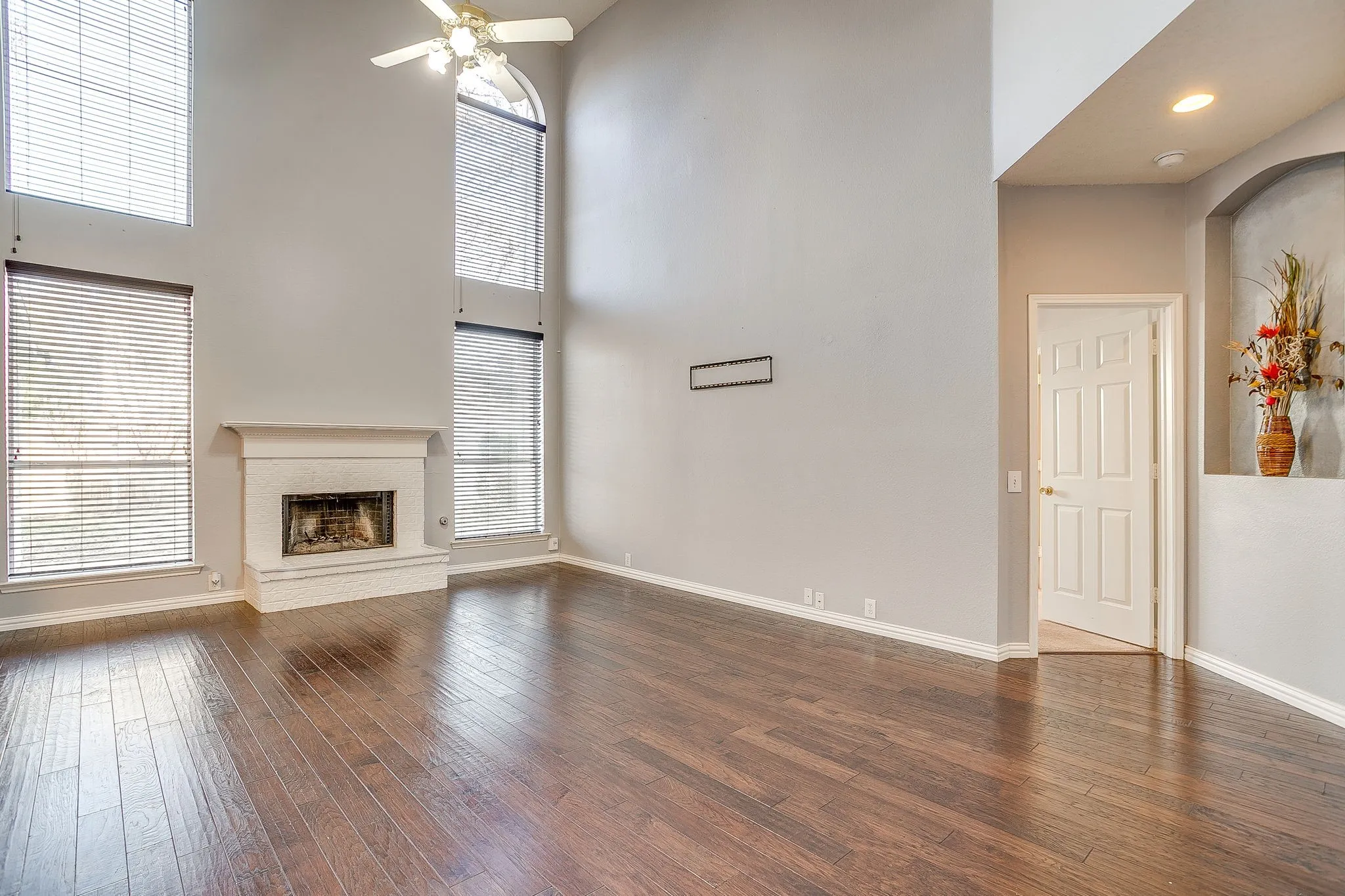 Unfurnished living room featuring a ceiling fan, a high ceiling, dark wood-style floors, and a brick fireplace