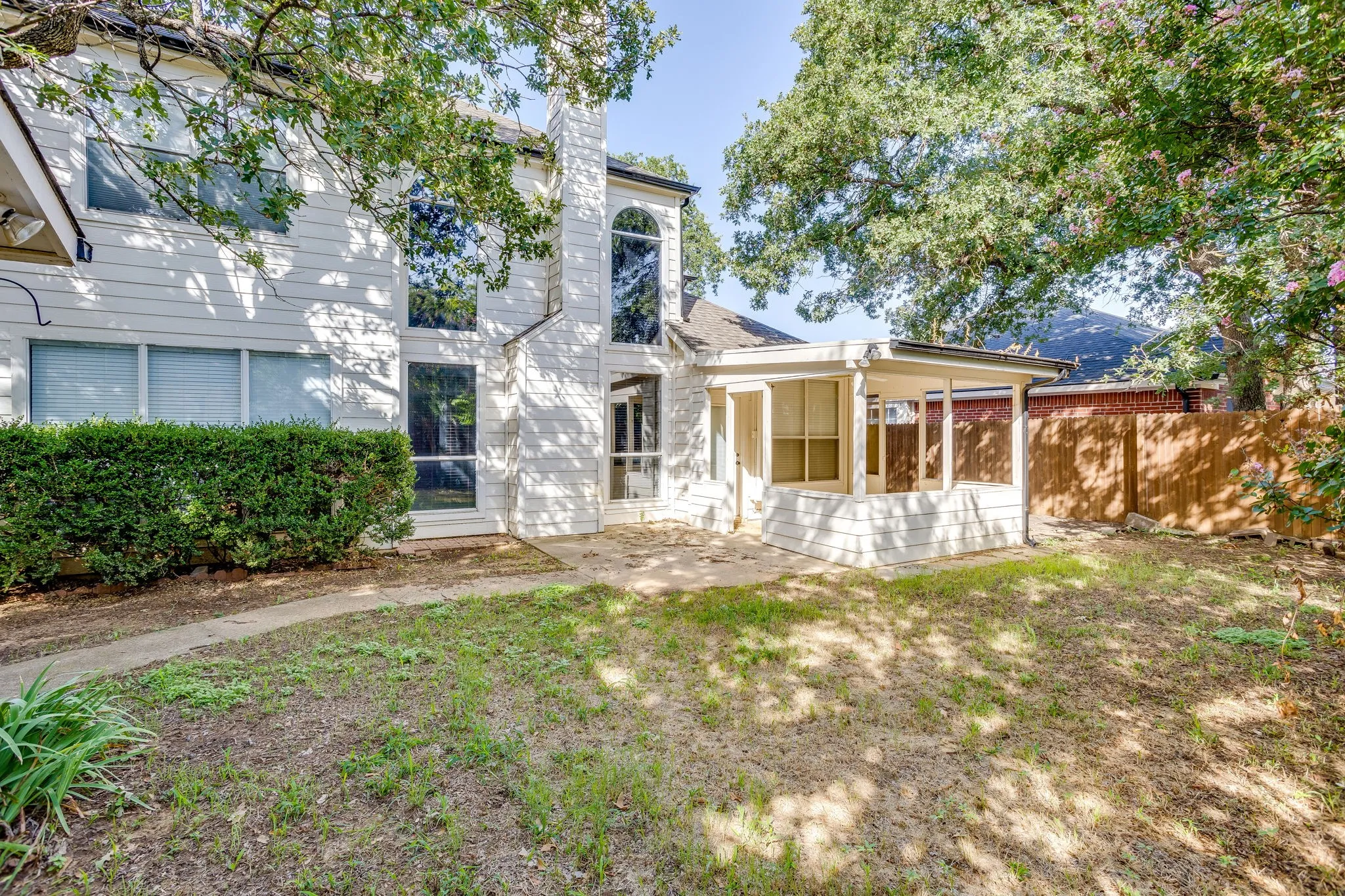 Expansive backyard patio featuring a covered porch, white siding exterior, and tall privacy fencing