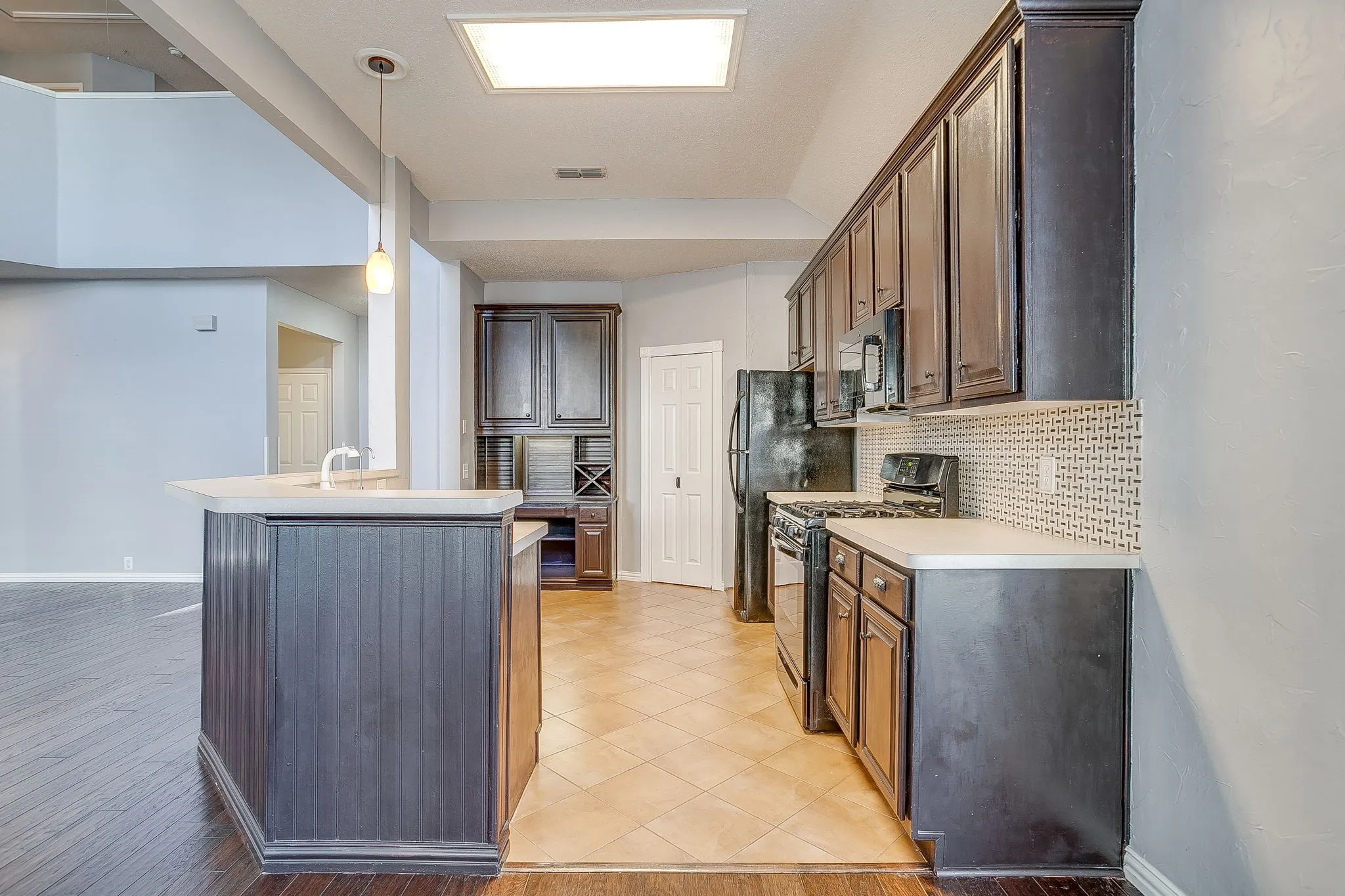 Kitchen featuring black gas range oven, light countertops, decorative light fixtures, backsplash, and light tile patterned floors