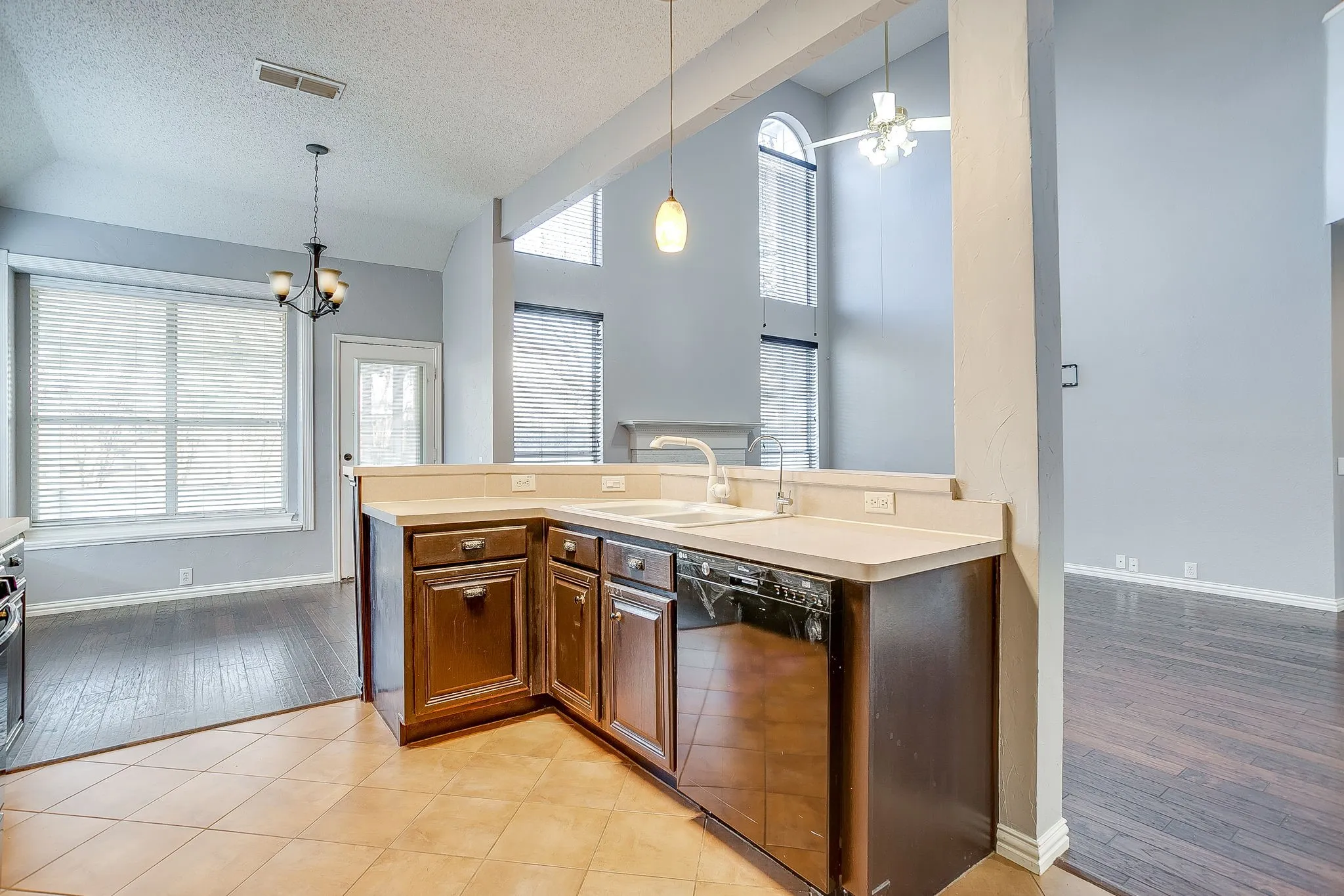 Kitchen with hanging lights, light countertops, dishwasher, a high textured ceiling, and dark wood finish cabinetry