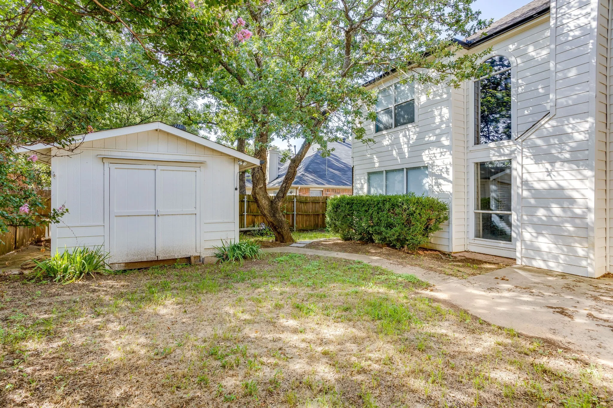 Backyard featuring a white storage shed with double doors, mature trees, and a wooden privacy fence