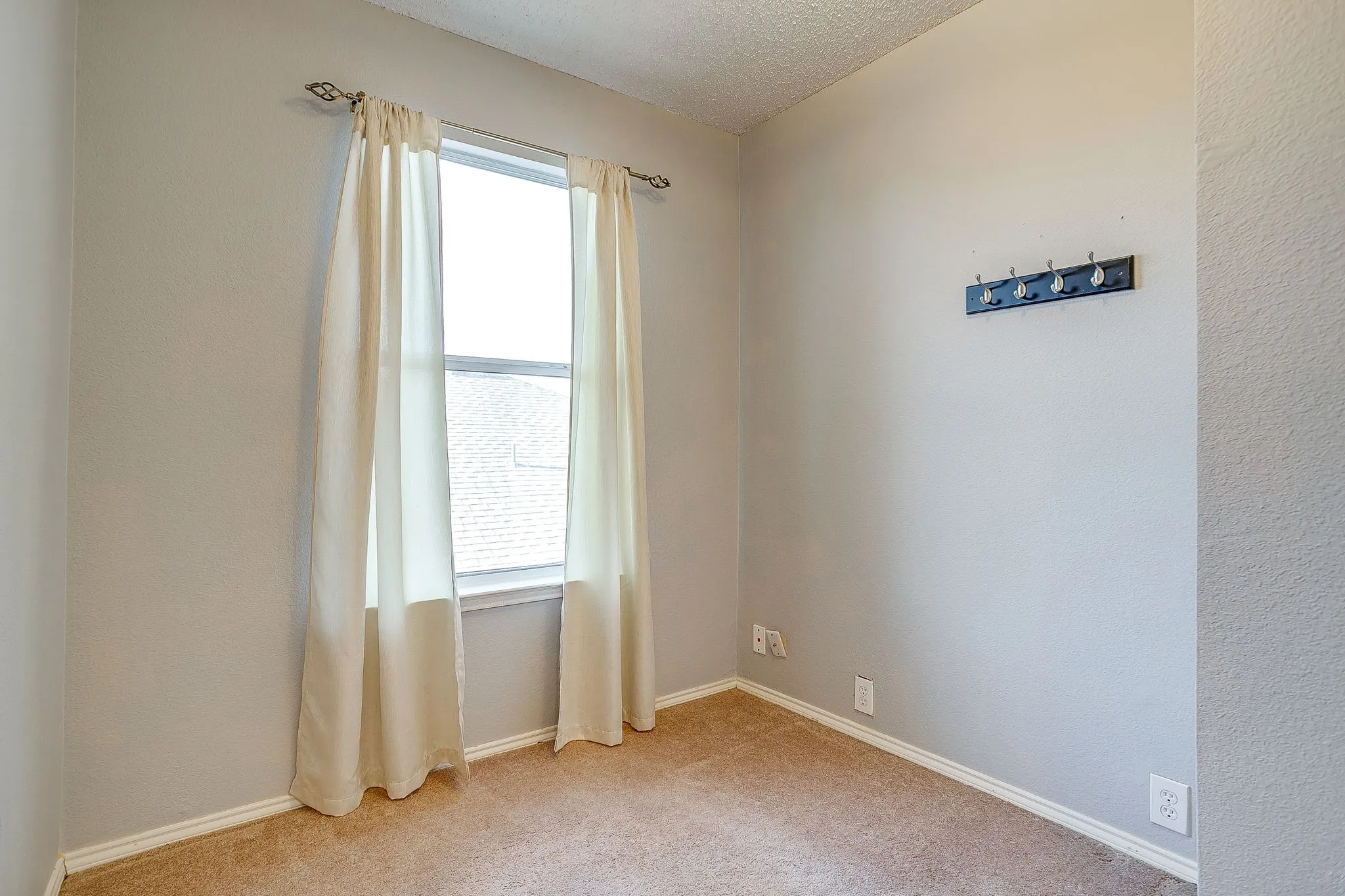 Empty room with light colored carpet, a textured ceiling, and a textured wall