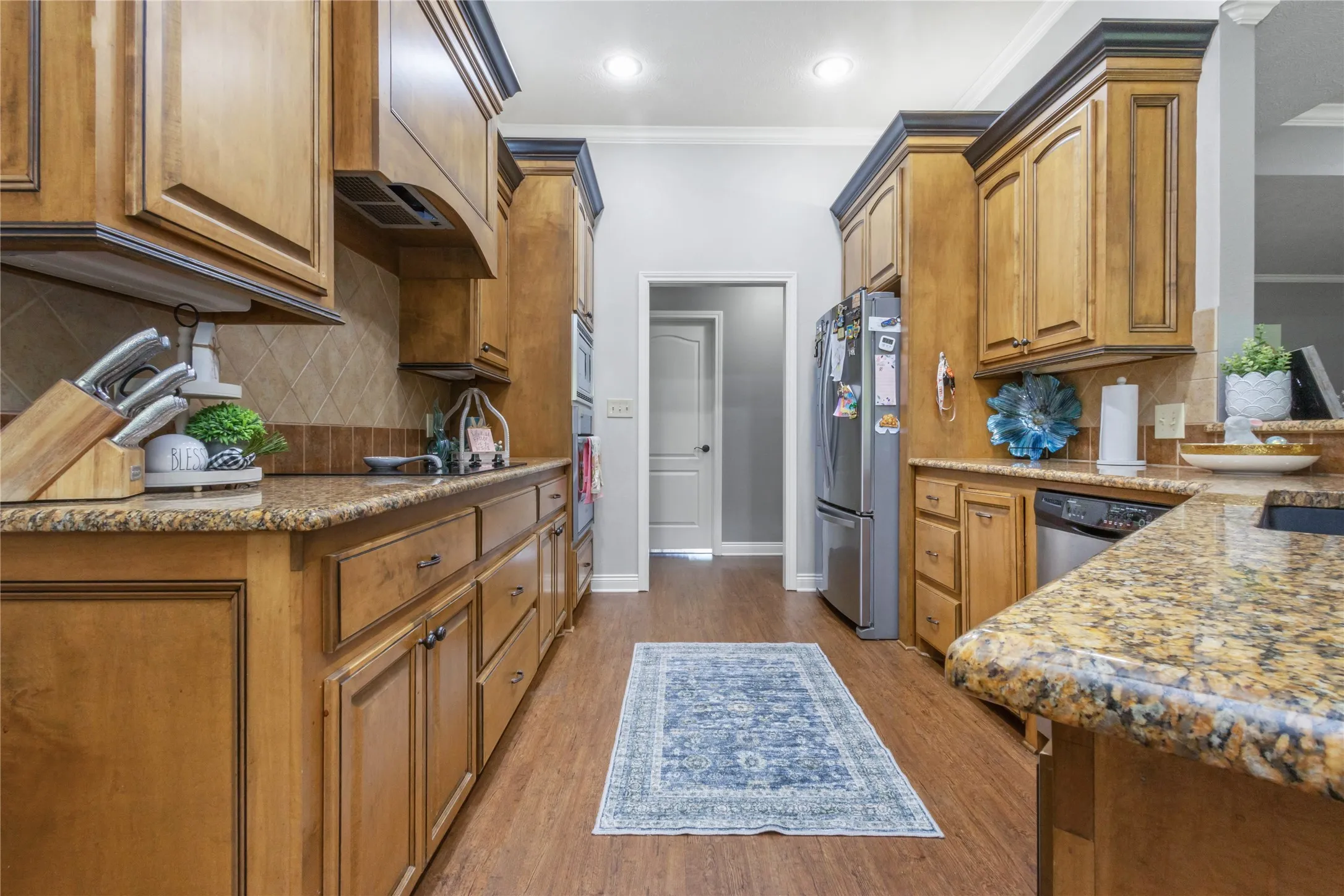 Kitchen featuring light stone counters, wood finish cabinets, stainless steel appliances, light wood-style floors, and backsplash