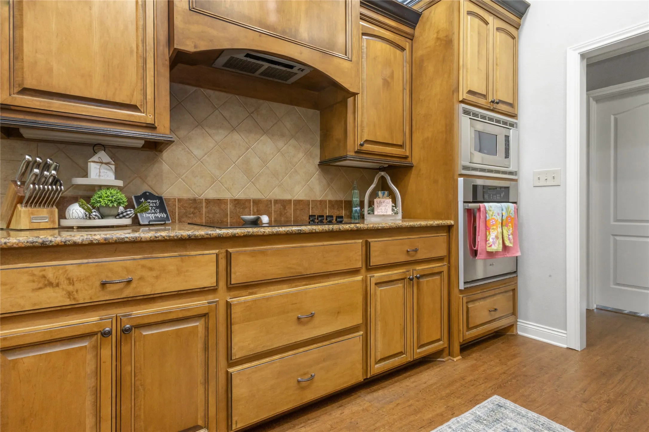 Kitchen featuring light stone counters, wood finish cabinets, stainless steel appliances, light wood-style floors, and backsplash