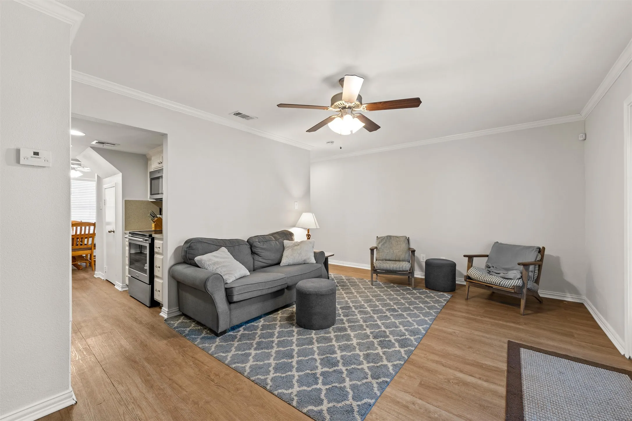 Vinyl plank flooring, ceiling fan with light fixture, crown molding, and French doors to the balcony and courtyard.