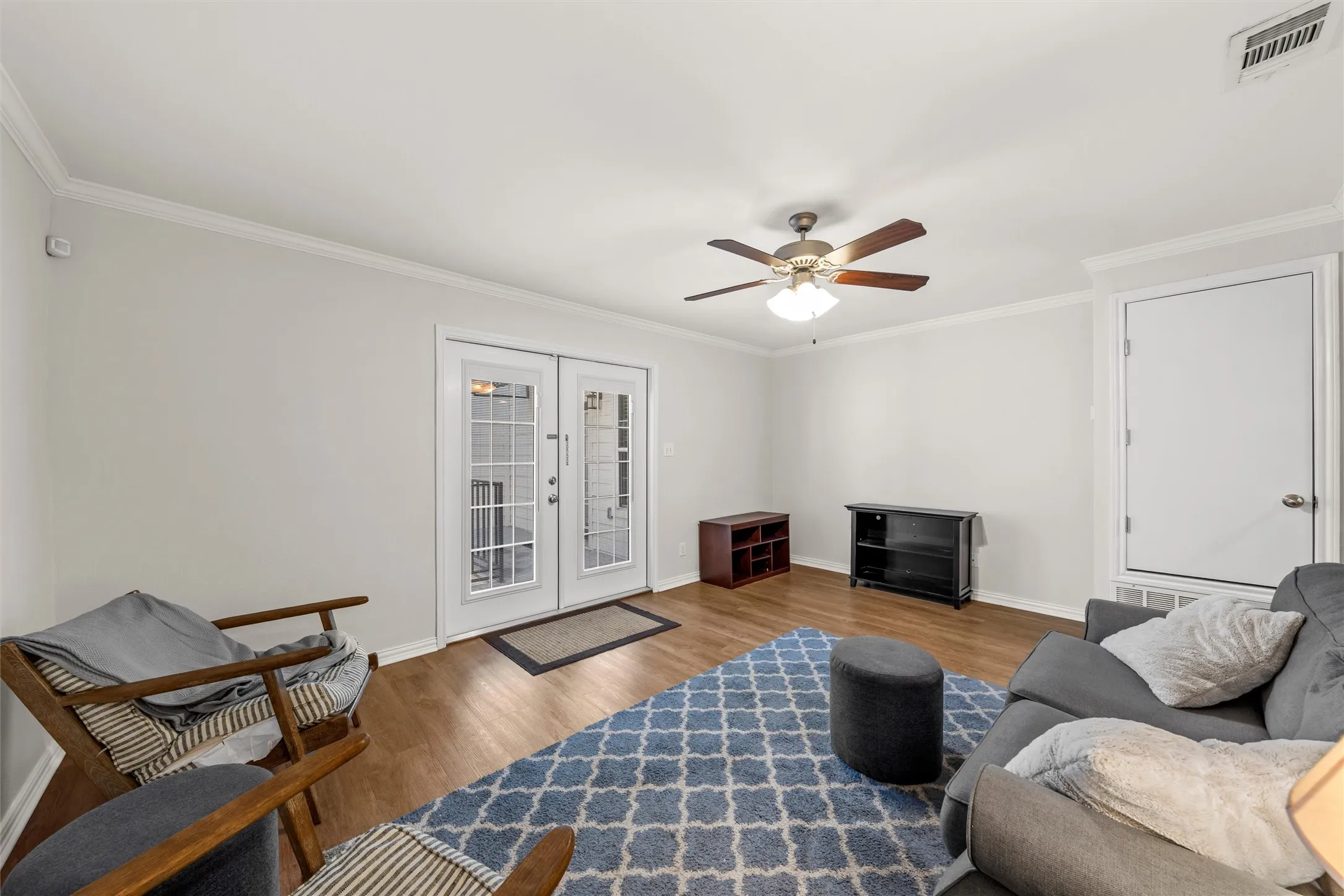 Vinyl plank flooring, ceiling fan with light fixture, crown molding, and French doors to the balcony and courtyard.