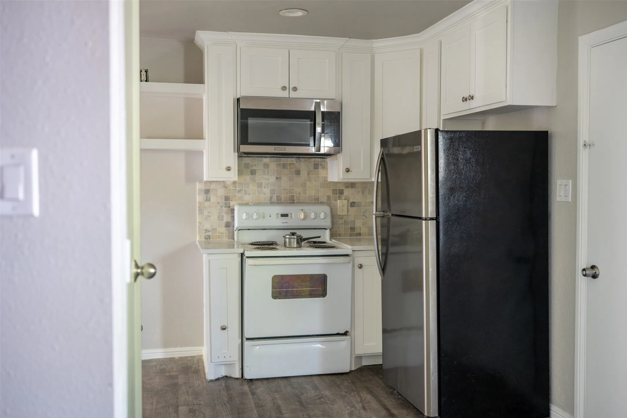 Kitchen featuring stainless steel appliances, white cabinetry, light countertops, dark wood-style floors, and backsplash