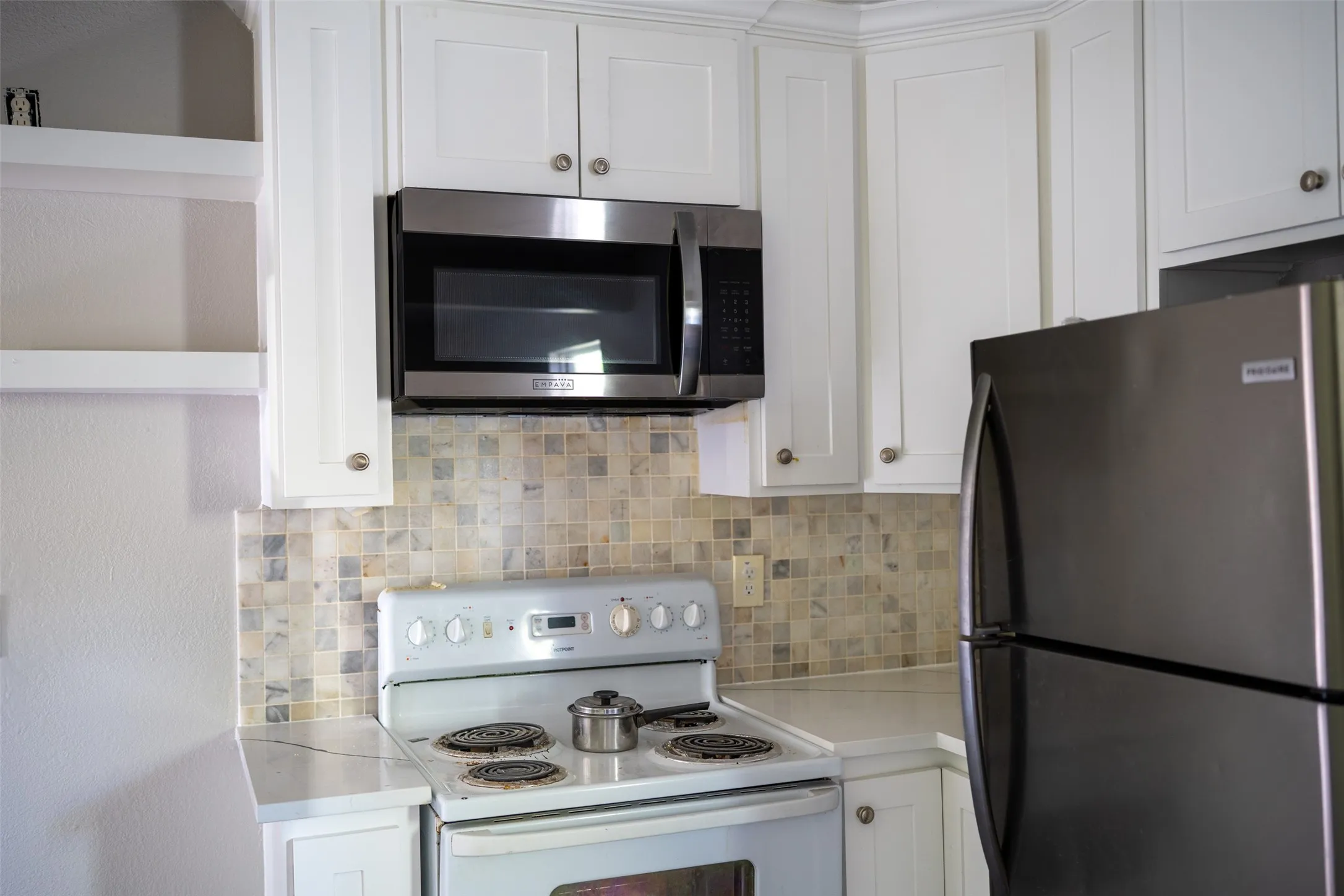 Kitchen featuring stainless steel appliances, white cabinets, light countertops, and tasteful backsplash