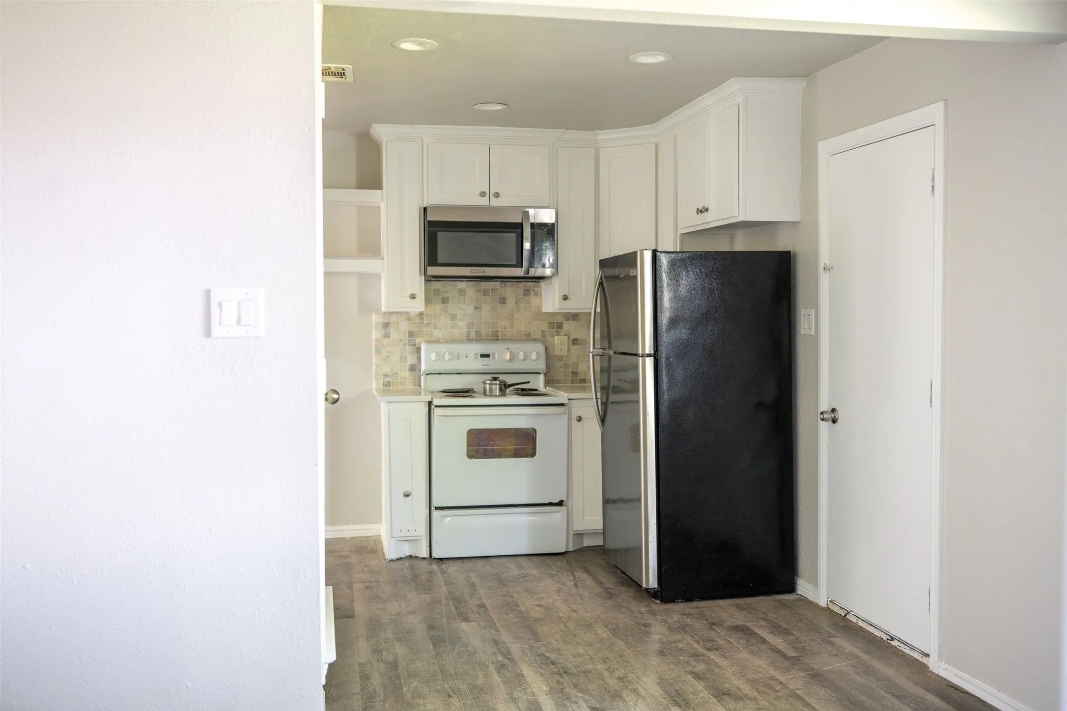Kitchen with stainless steel appliances, white cabinetry, light countertops, dark wood-style floors, and backsplash