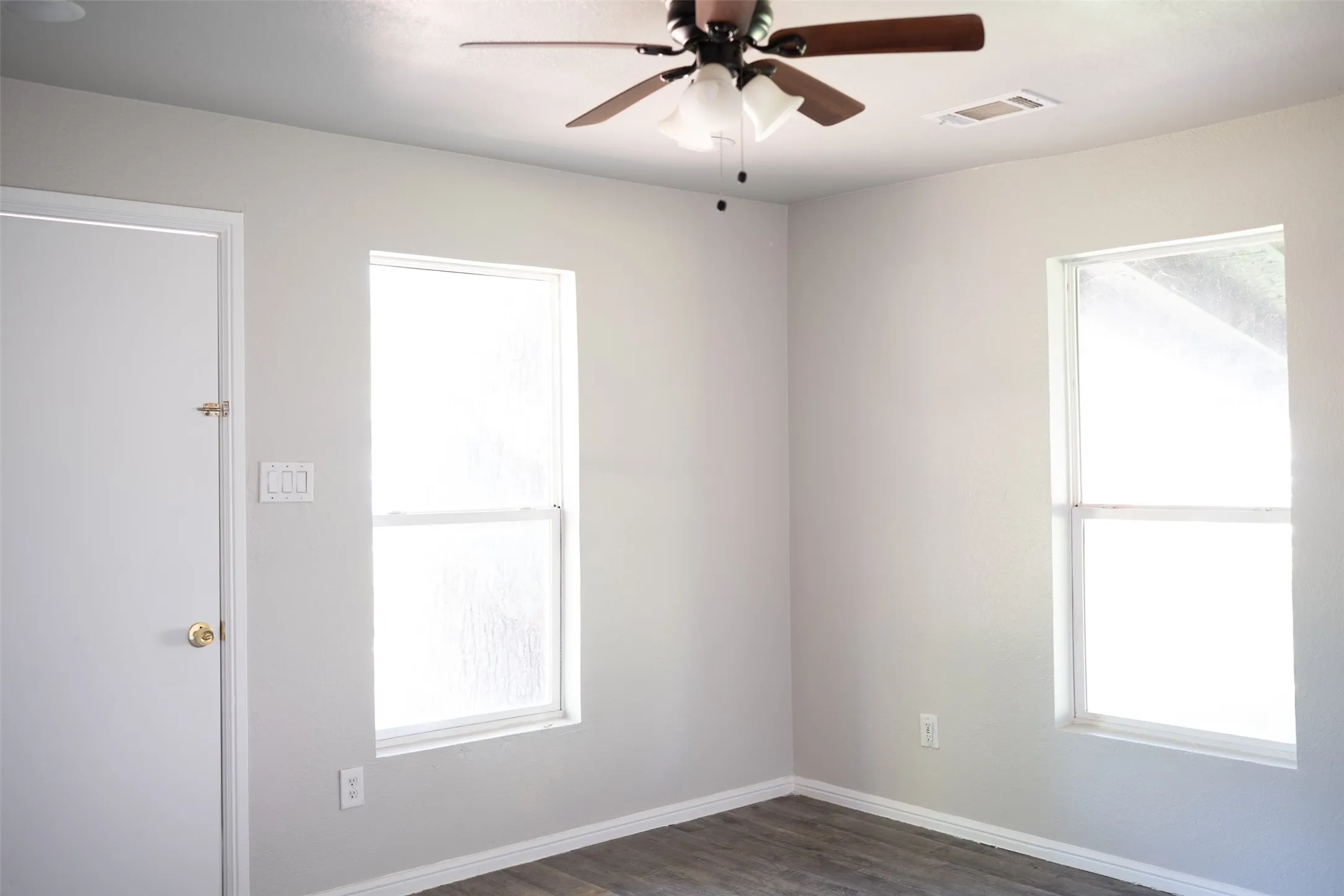 Unfurnished room featuring a ceiling fan, dark wood-style flooring, and plenty of natural light
