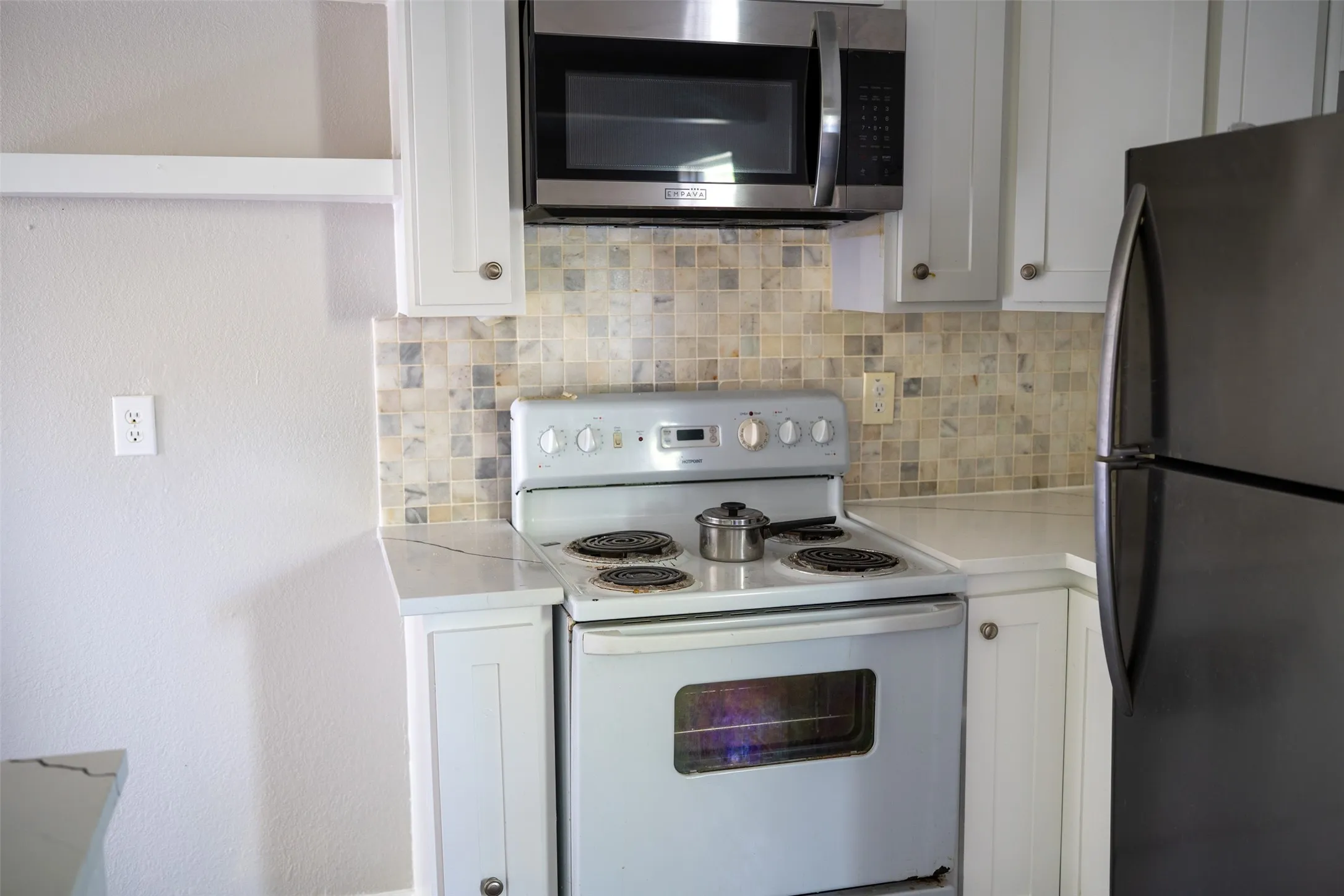 Kitchen featuring stainless steel appliances, white cabinetry, and decorative backsplash